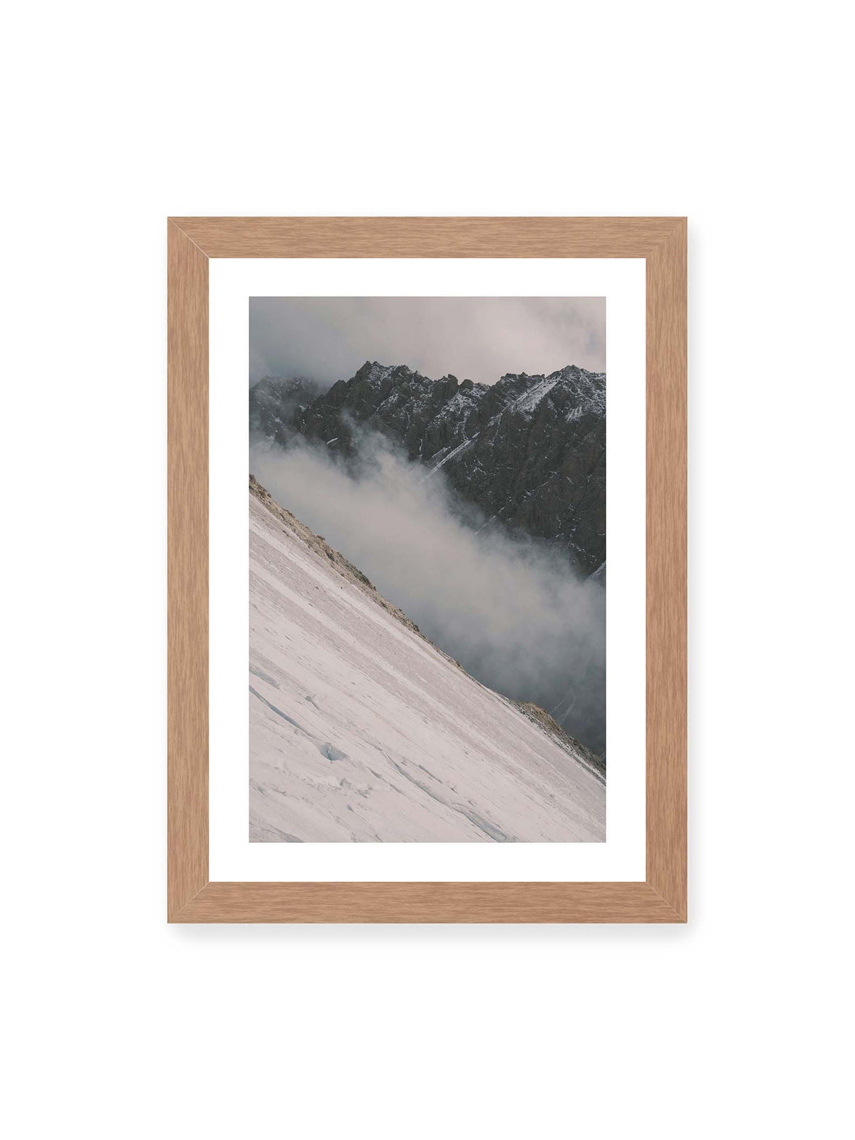 21x30 cm, weißer Galerie-Rand, Eichenrahmen – Diagonale Schneefläche vor dunkler Felswand, durchzogen von tief liegenden Wolken.