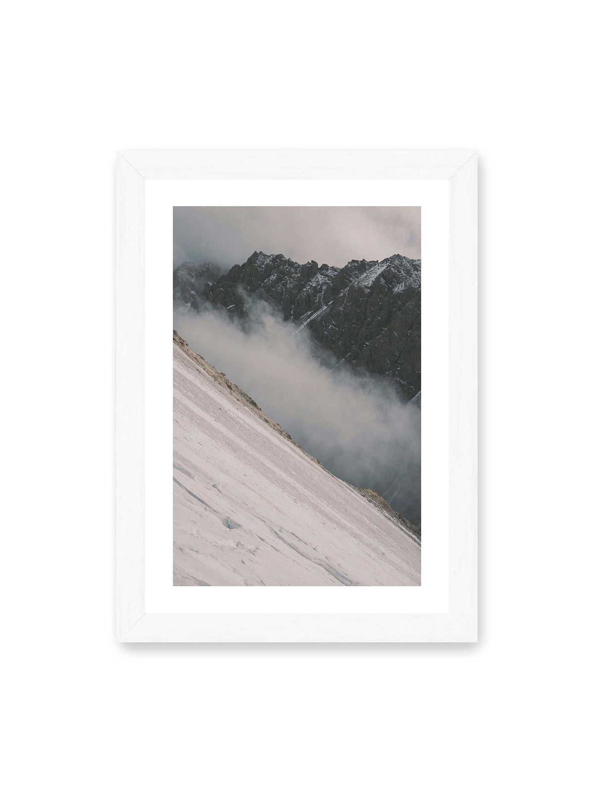 21x30 cm, weißer Galerie-Rand, weißer Rahmen – Diagonale Schneefläche vor dunkler Felswand, durchzogen von tief liegenden Wolken.