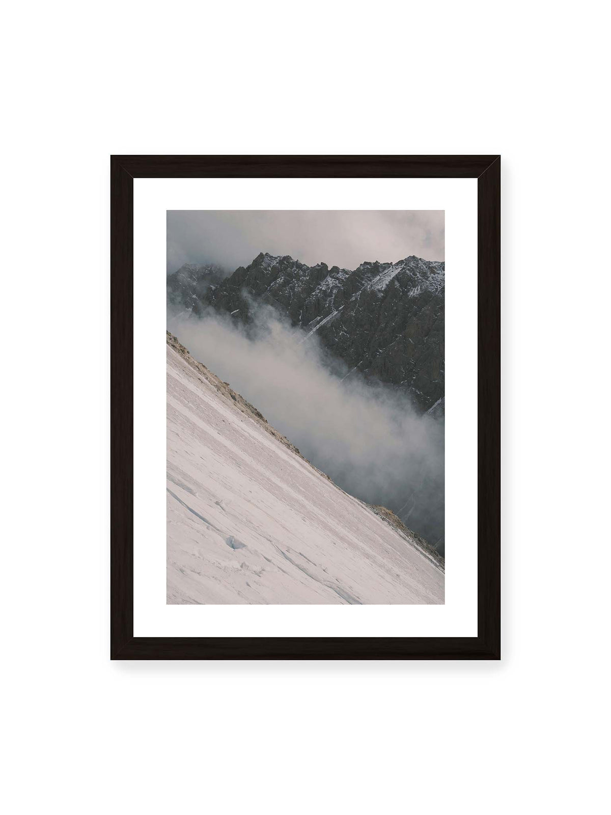 30x40 cm, weißer Galerie-Rand, schwarzer Rahmen – Diagonale Schneefläche vor dunkler Felswand, durchzogen von tief liegenden Wolken.