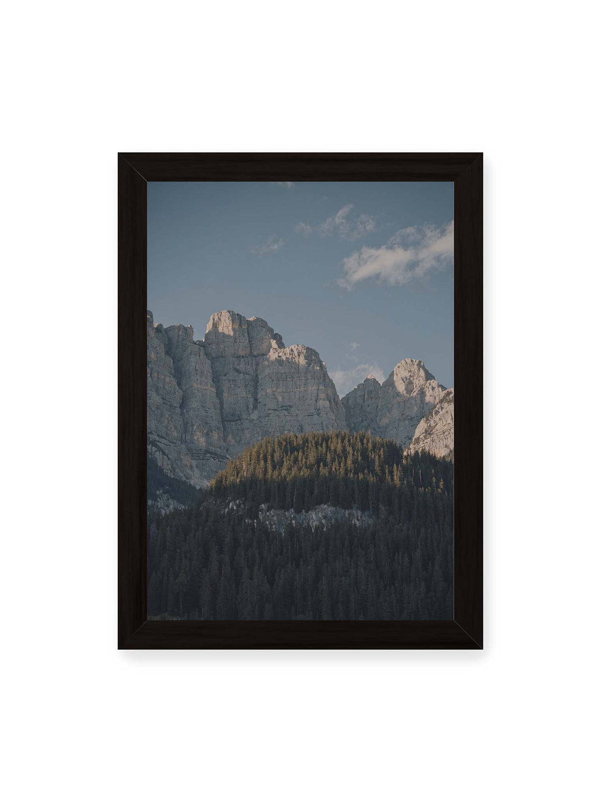 21x30 cm, schwarzer Rahmen – Helle Felswände erheben sich über einem dunklen Nadelwald vor klarem blauem Himmel.