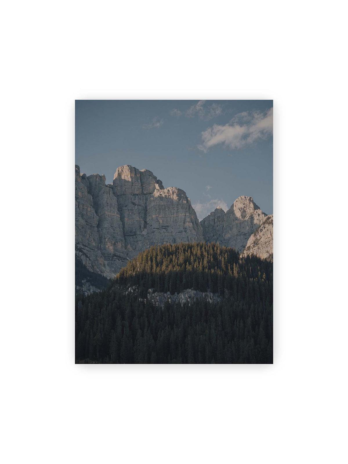 30x40 cm – Helle Felswände erheben sich über einem dunklen Nadelwald vor klarem blauem Himmel.