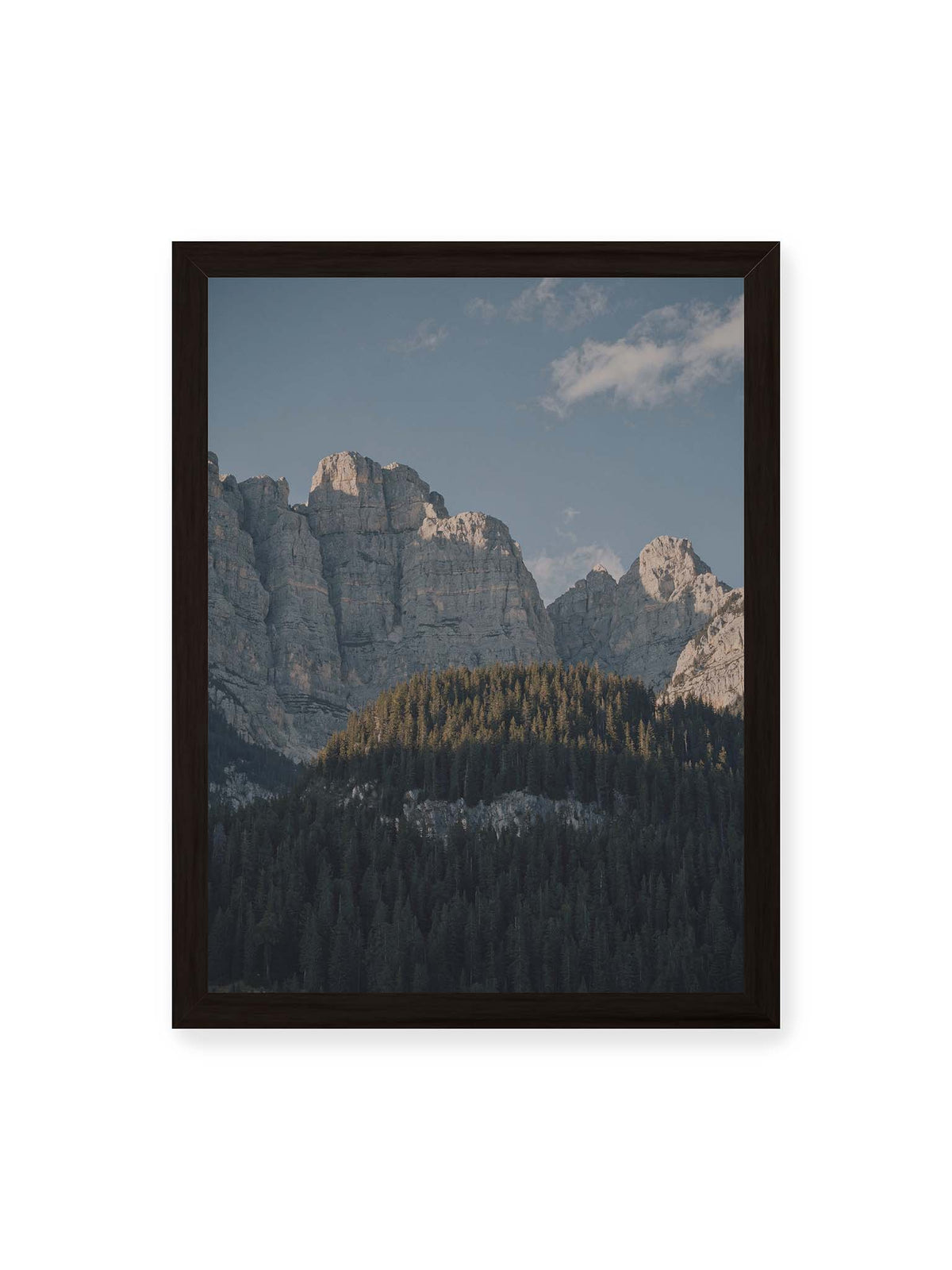 30x40 cm, schwarzer Rahmen – Helle Felswände erheben sich über einem dunklen Nadelwald vor klarem blauem Himmel.