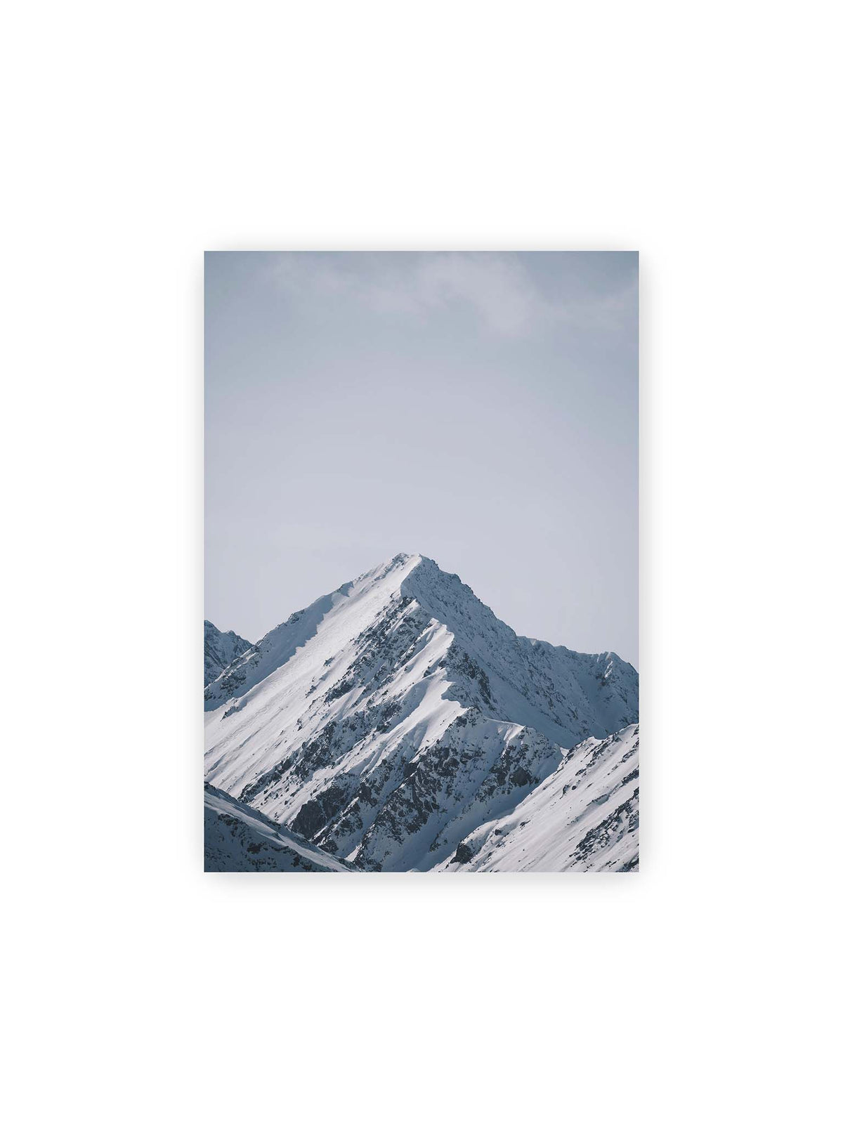 21x30 cm – Schneebedeckter Berggipfel mit steilen Graten vor einem weiten blassblauen Himmel.