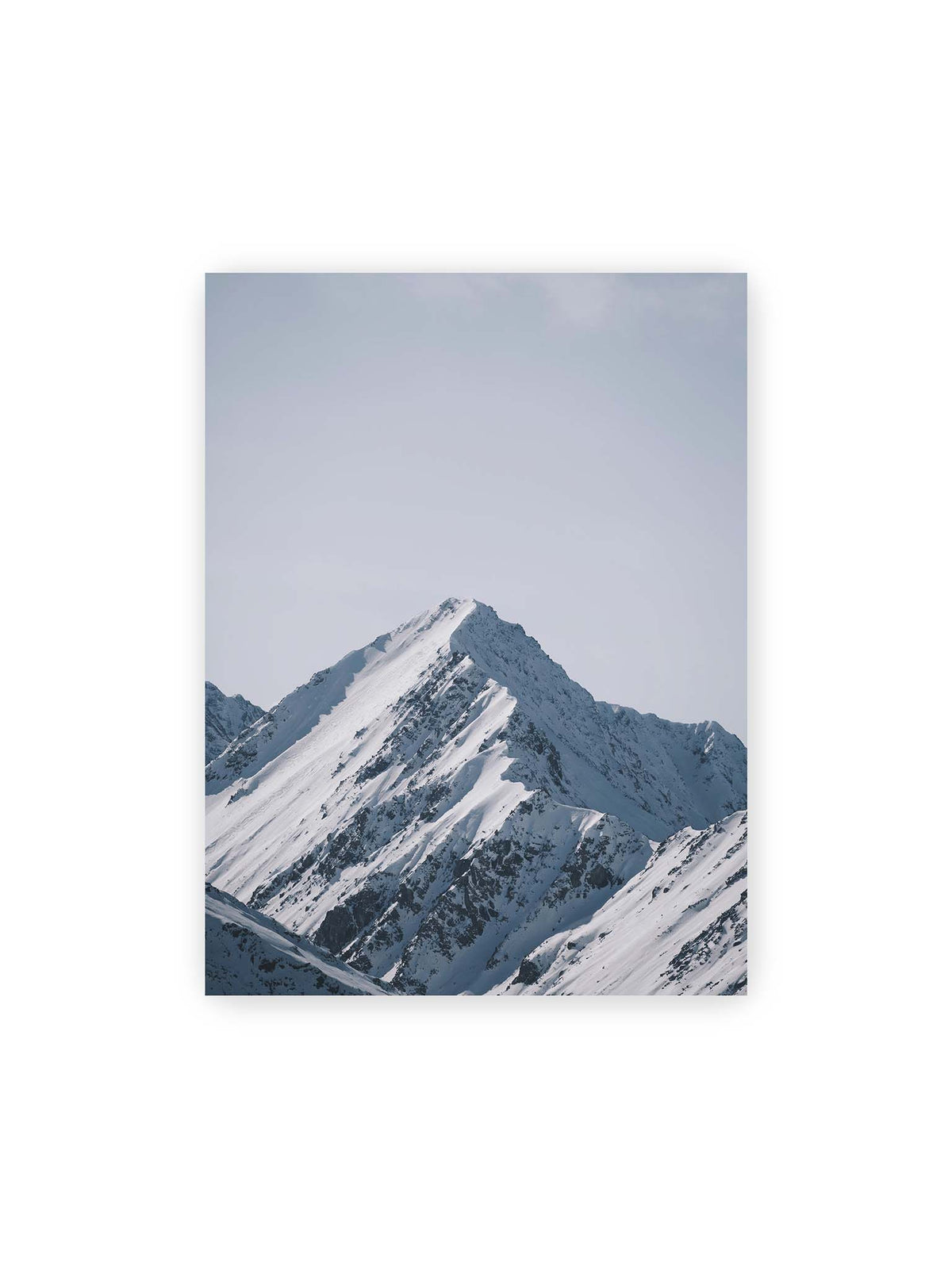 30x40 cm – Schneebedeckter Berggipfel mit steilen Graten vor einem weiten blassblauen Himmel.