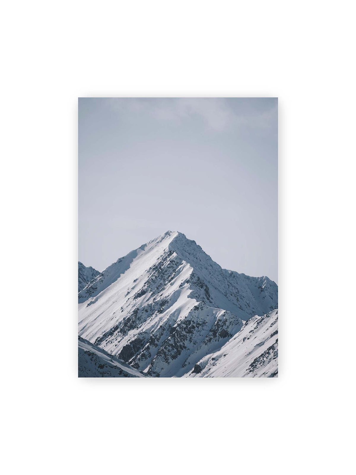 50x70 cm – Schneebedeckter Berggipfel mit steilen Graten vor einem weiten blassblauen Himmel.