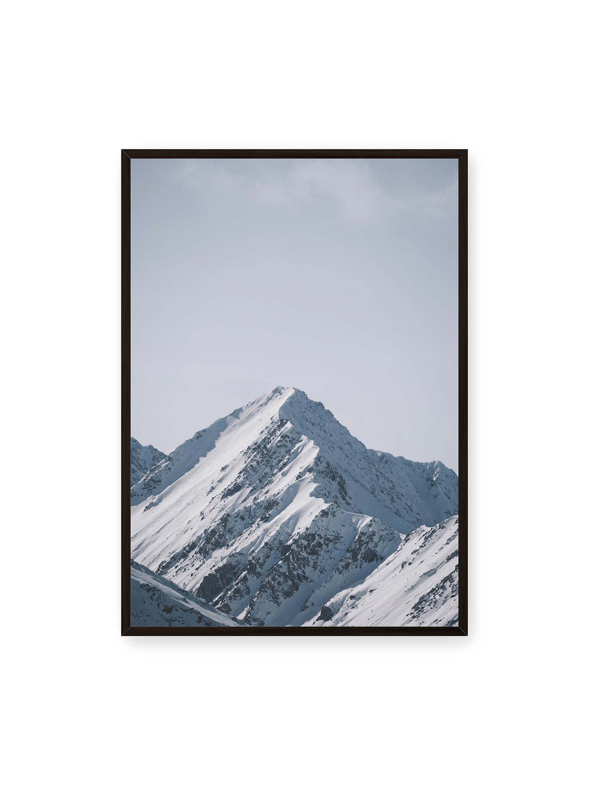70x100 cm, schwarzer Rahmen – Schneebedeckter Berggipfel mit steilen Graten vor einem weiten blassblauen Himmel.