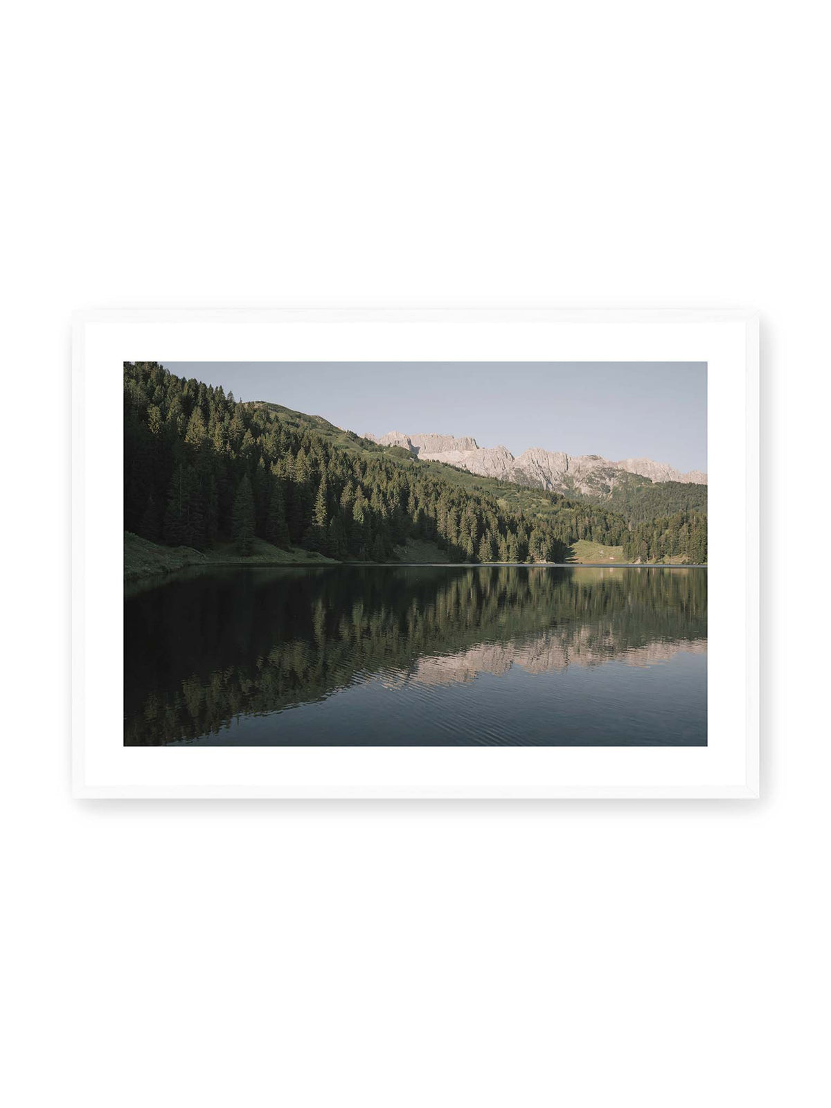 100x70 cm, weißer Galerie-Rand, weißer Rahmen – Ruhiger Bergsee mit Spiegelungen von bewaldeten Hängen und einer hellen Felskette unter blauem Himmel.