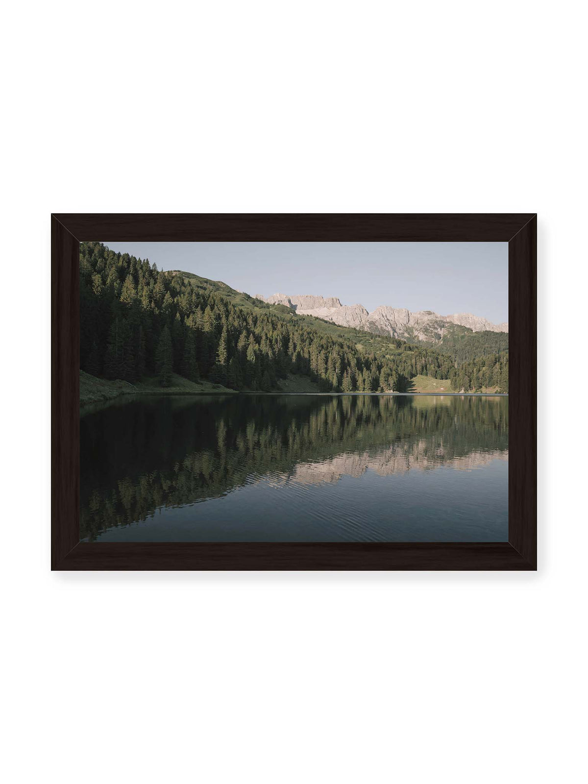 30x21 cm, schwarzer Rahmen – Ruhiger Bergsee mit Spiegelungen von bewaldeten Hängen und einer hellen Felskette unter blauem Himmel.