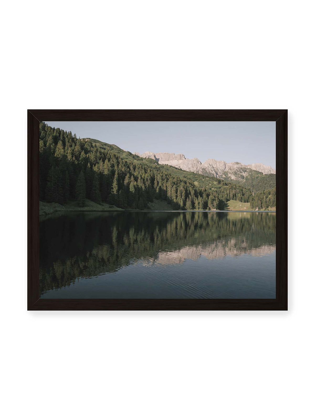 40x30 cm, schwarzer Rahmen – Ruhiger Bergsee mit Spiegelungen von bewaldeten Hängen und einer hellen Felskette unter blauem Himmel.