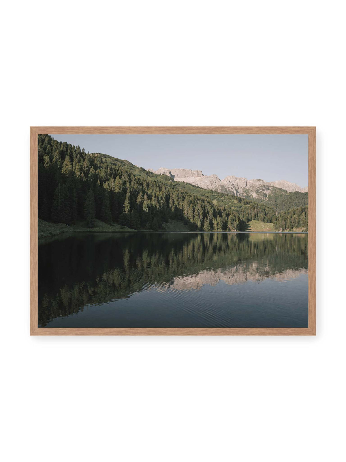 70x50 cm, Eichenrahmen – Ruhiger Bergsee mit Spiegelungen von bewaldeten Hängen und einer hellen Felskette unter blauem Himmel.