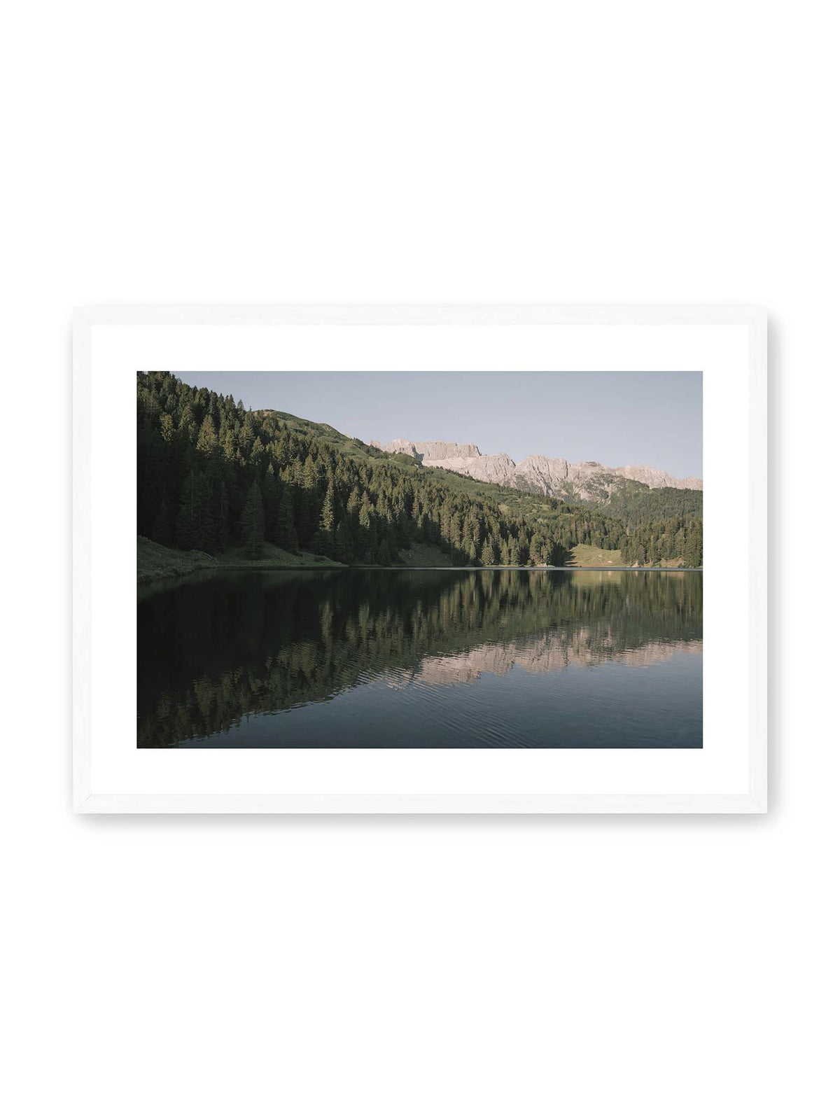 70x50 cm, weißer Galerie-Rand, weißer Rahmen – Ruhiger Bergsee mit Spiegelungen von bewaldeten Hängen und einer hellen Felskette unter blauem Himmel.