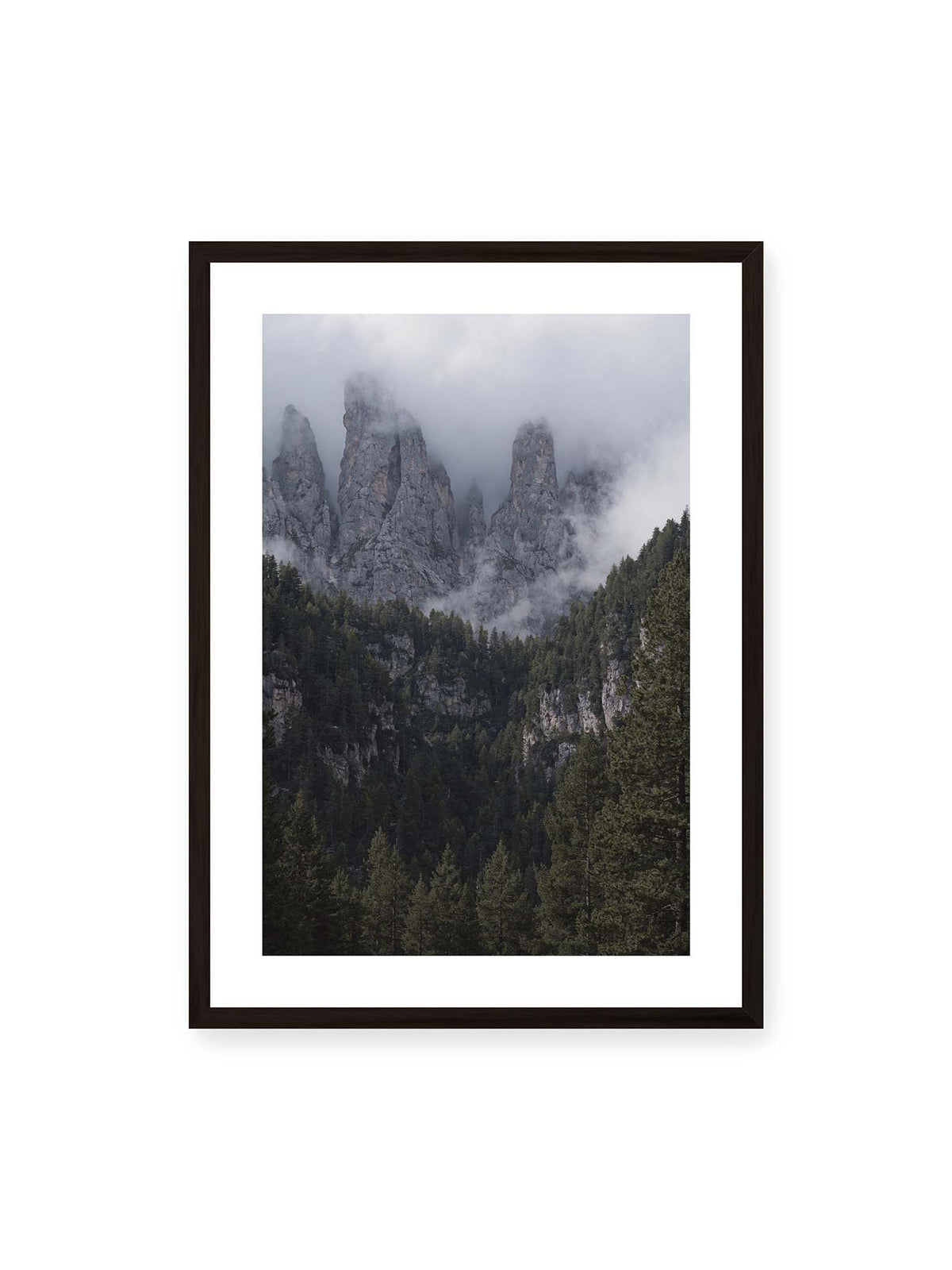 50x70 cm, weißer Galerie-Rand, schwarzer Rahmen – Steile graue Felstürme zwischen tiefen Wolken über einem dicht bewachsenen dunklen Nadelwald.