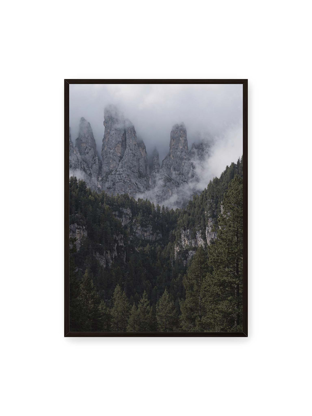 70x100 cm, schwarzer Rahmen – Steile graue Felstürme zwischen tiefen Wolken über einem dicht bewachsenen dunklen Nadelwald.
