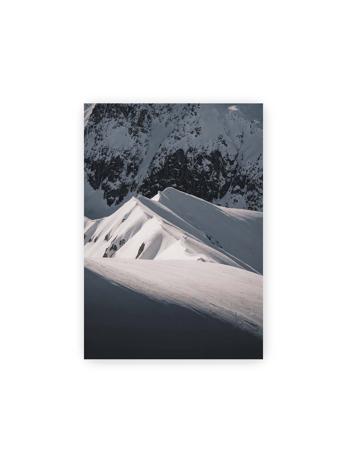 21x30 cm – Schneebedeckte Berggrate mit scharfen Kämmen und tiefen Schatten vor einer dunklen felsigen Bergwand.