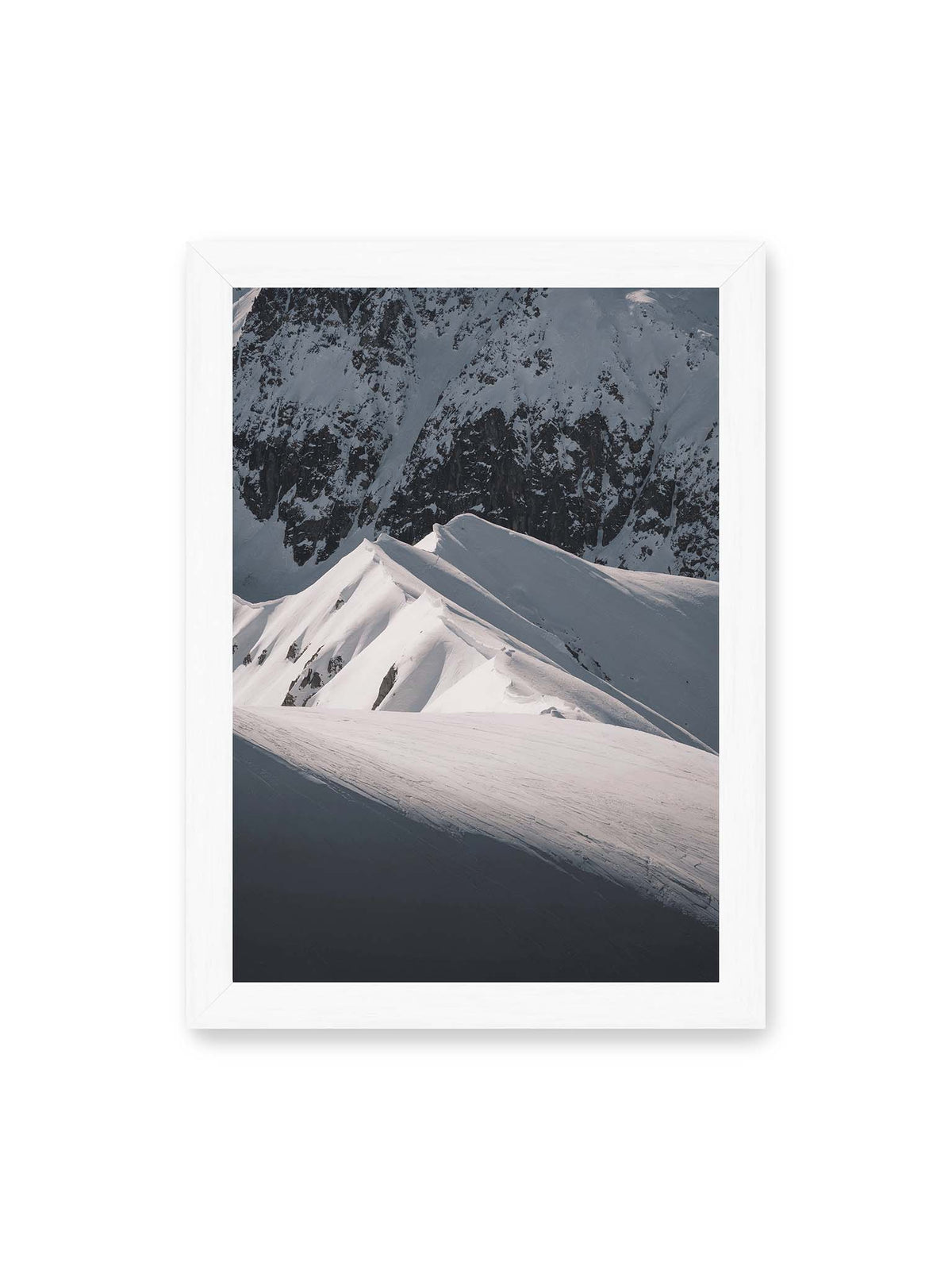 21x30 cm, weißer Rahmen – Schneebedeckte Berggrate mit scharfen Kämmen und tiefen Schatten vor einer dunklen felsigen Bergwand.
