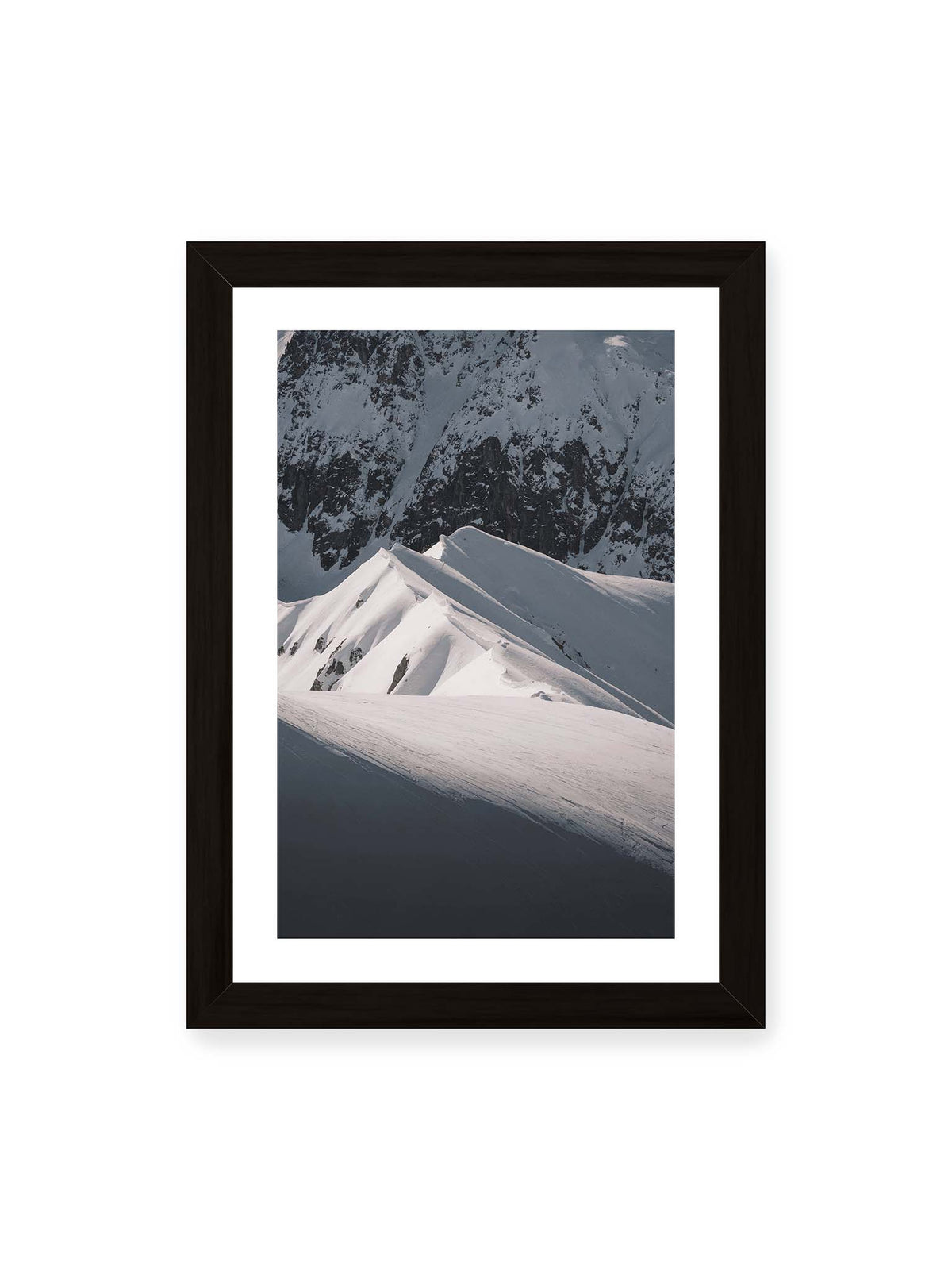 21x30 cm, weißer Galerie-Rand, schwarzer Rahmen – Schneebedeckte Berggrate mit scharfen Kämmen und tiefen Schatten vor einer dunklen felsigen Bergwand.