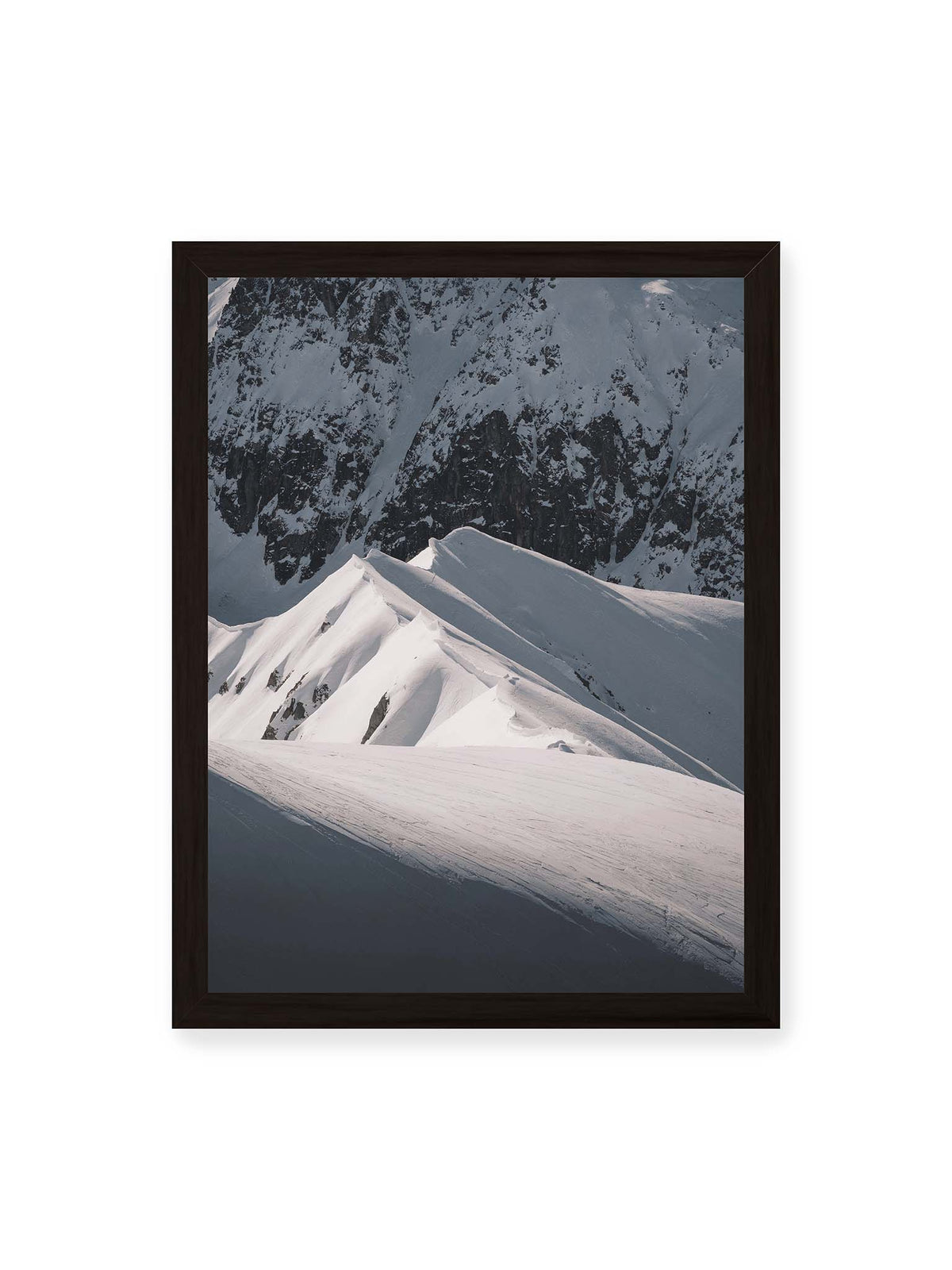 30x40 cm, schwarzer Rahmen – Schneebedeckte Berggrate mit scharfen Kämmen und tiefen Schatten vor einer dunklen felsigen Bergwand.