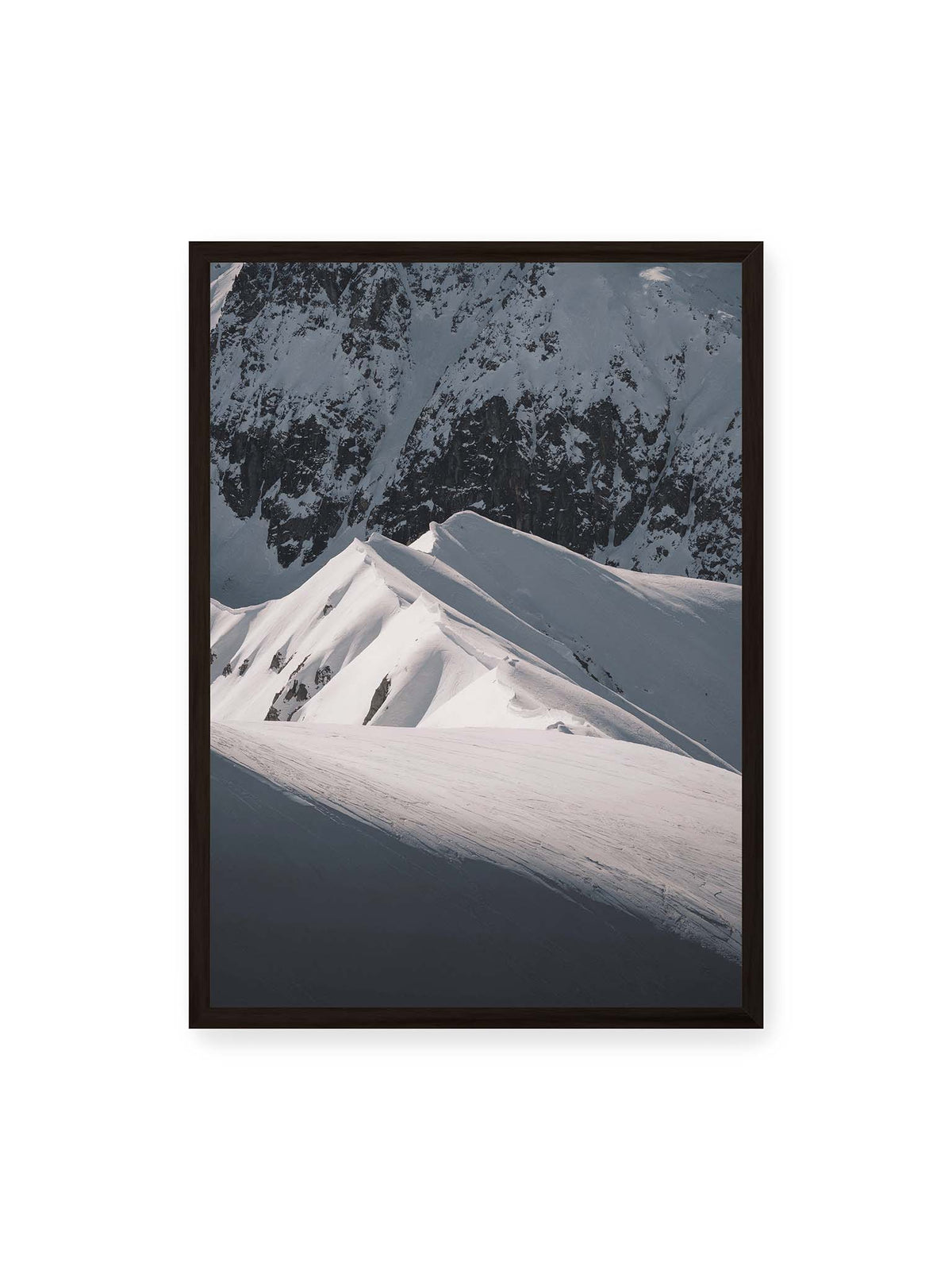 50x70 cm, schwarzer Rahmen – Schneebedeckte Berggrate mit scharfen Kämmen und tiefen Schatten vor einer dunklen felsigen Bergwand.