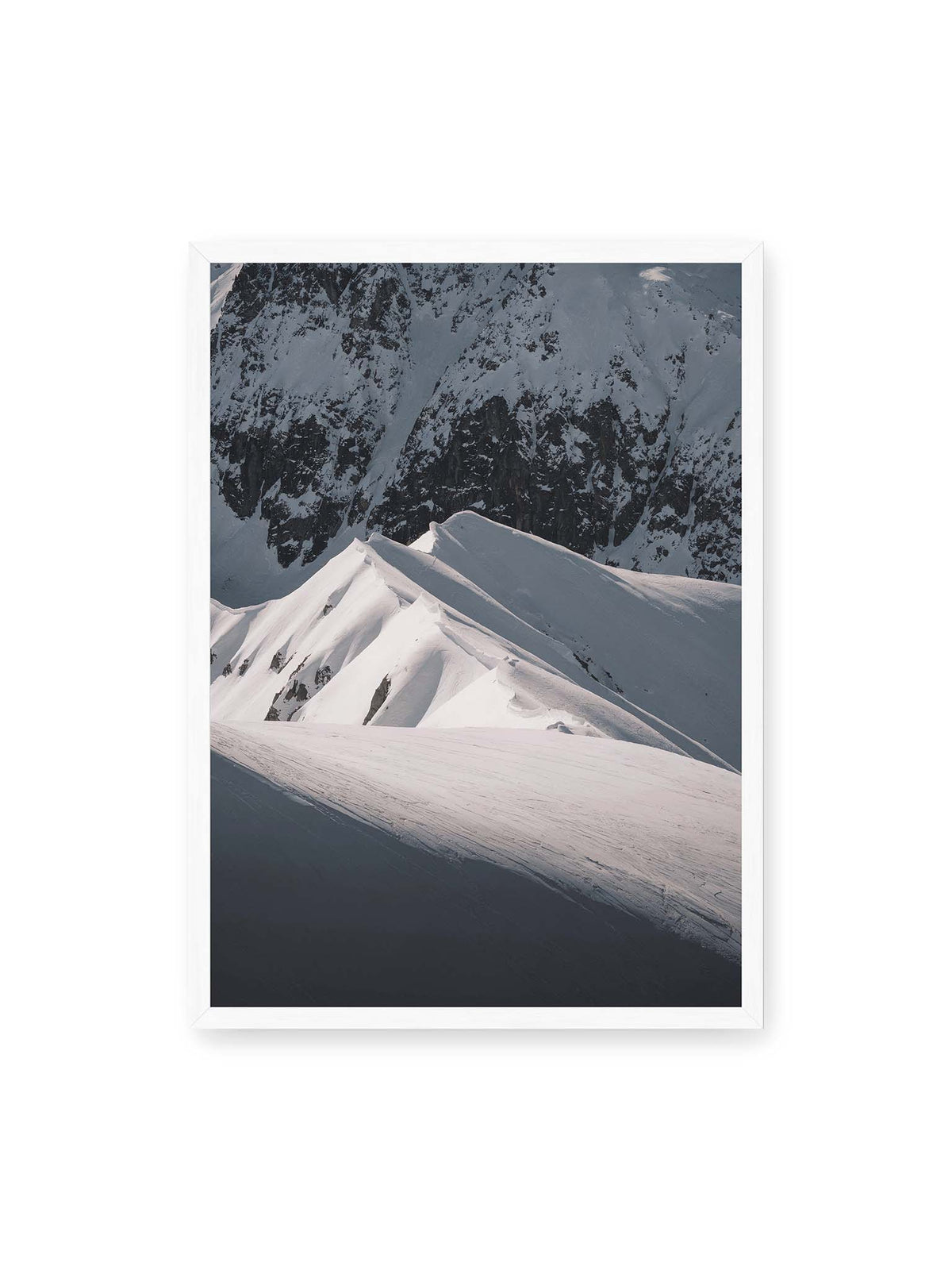 50x70 cm, weißer Rahmen – Schneebedeckte Berggrate mit scharfen Kämmen und tiefen Schatten vor einer dunklen felsigen Bergwand.