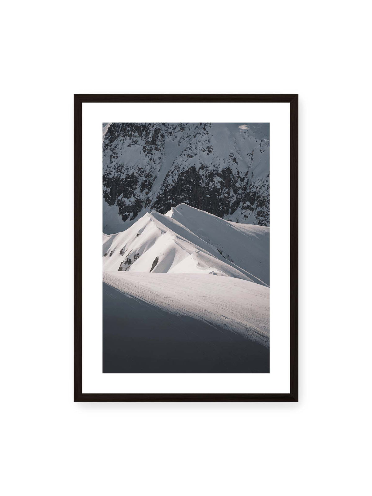 50x70 cm, weißer Galerie-Rand, schwarzer Rahmen – Schneebedeckte Berggrate mit scharfen Kämmen und tiefen Schatten vor einer dunklen felsigen Bergwand.