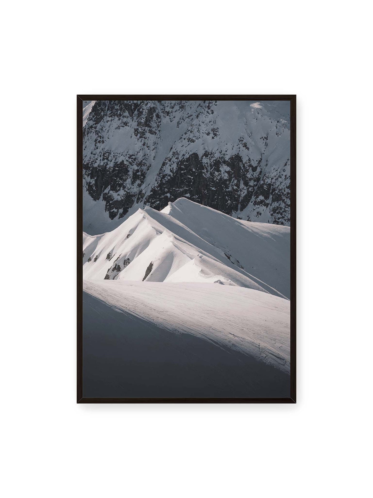 70x100 cm, schwarzer Rahmen – Schneebedeckte Berggrate mit scharfen Kämmen und tiefen Schatten vor einer dunklen felsigen Bergwand.