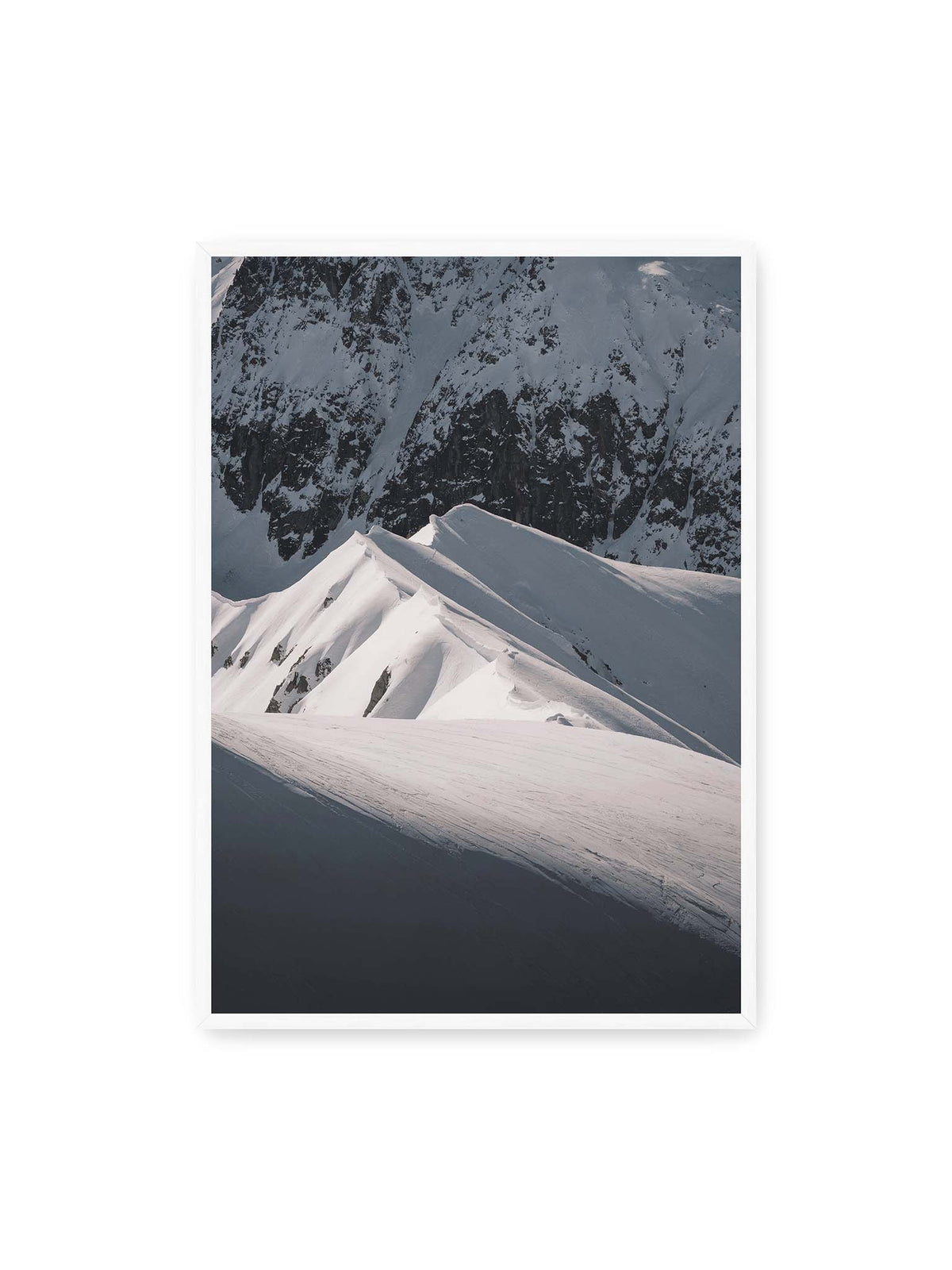 70x100 cm, weißer Rahmen – Schneebedeckte Berggrate mit scharfen Kämmen und tiefen Schatten vor einer dunklen felsigen Bergwand.