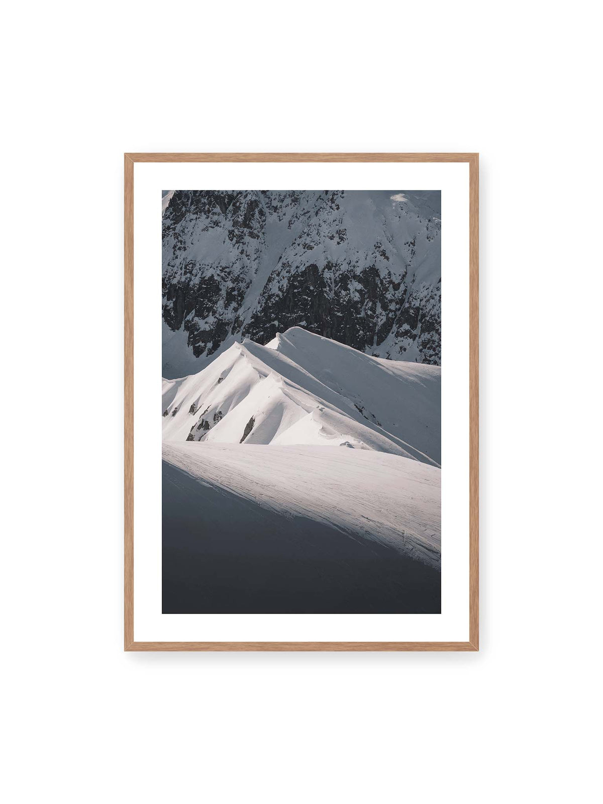 70x100 cm, weißer Galerie-Rand, Eichenrahmen – Schneebedeckte Berggrate mit scharfen Kämmen und tiefen Schatten vor einer dunklen felsigen Bergwand.
