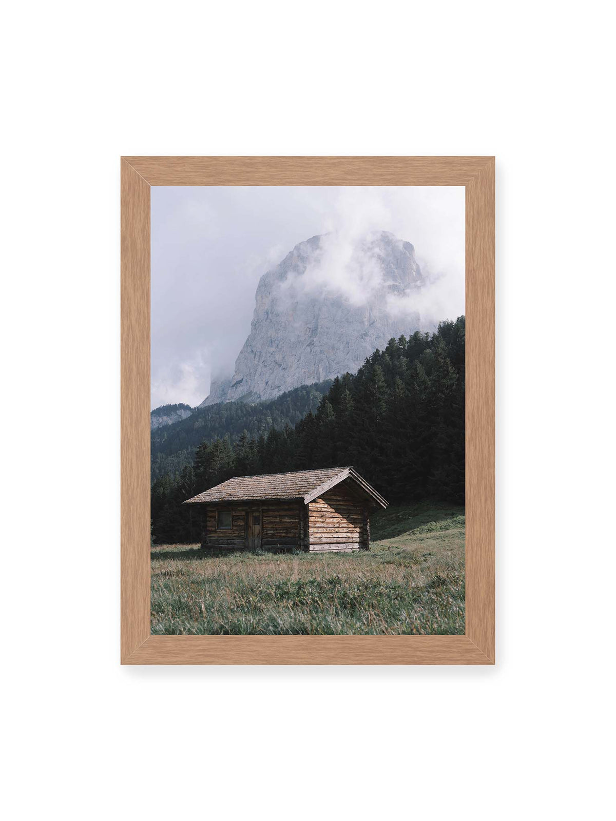 21x30 cm, Eichenrahmen – Holzhütte auf einer Wiese vor dichtem Nadelwald und einer hohen, teilweise von Wolken verhüllten Felswand.