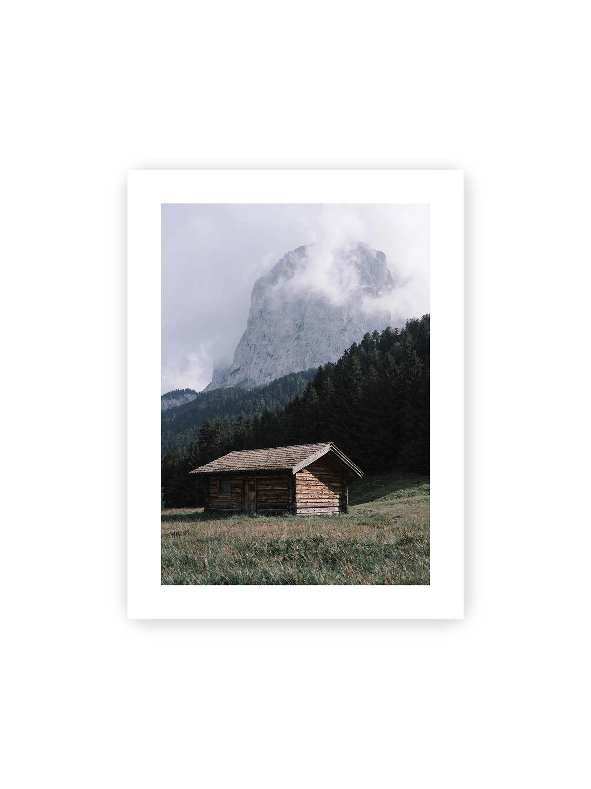 30x40 cm, weißer Galerie-Rand – Holzhütte auf einer Wiese vor dichtem Nadelwald und einer hohen, teilweise von Wolken verhüllten Felswand.
