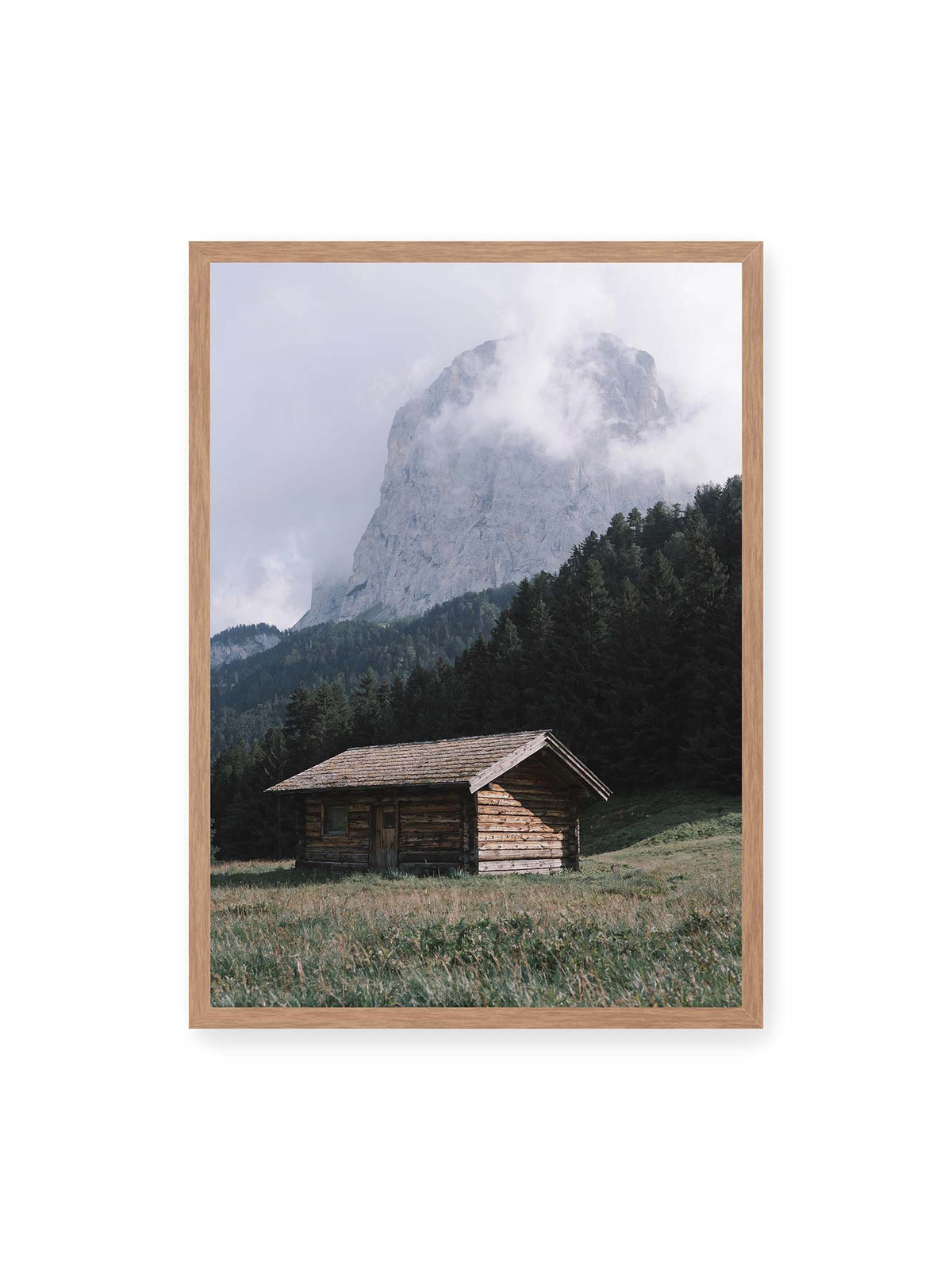 50x70 cm, Eichenrahmen – Holzhütte auf einer Wiese vor dichtem Nadelwald und einer hohen, teilweise von Wolken verhüllten Felswand.