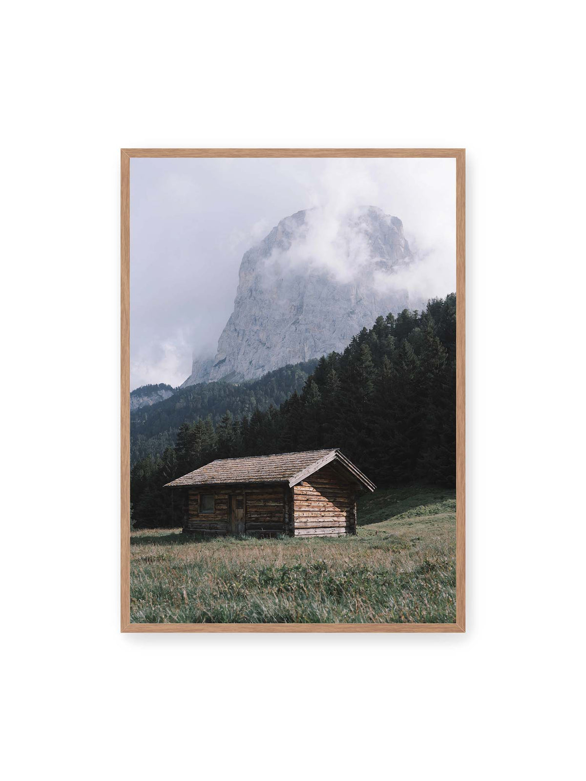70x100 cm, Eichenrahmen – Holzhütte auf einer Wiese vor dichtem Nadelwald und einer hohen, teilweise von Wolken verhüllten Felswand.