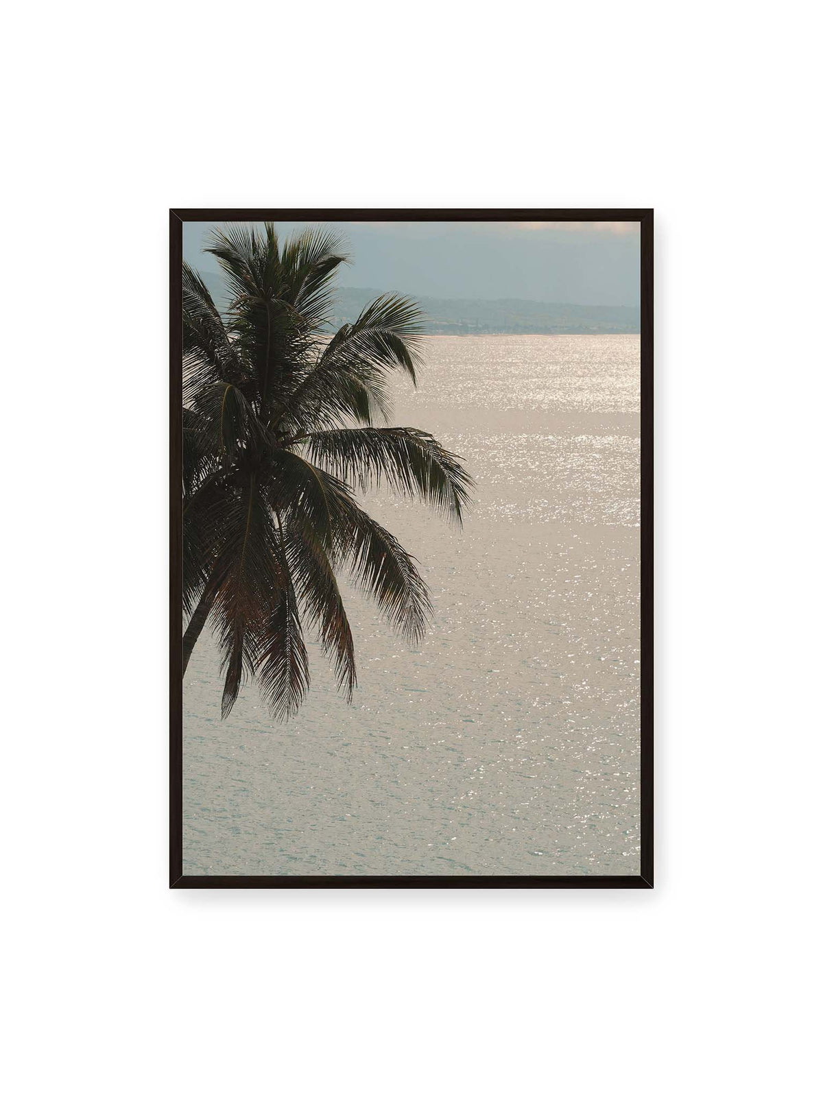 70x100 cm, schwarzer Rahmen – Dunkle Palmwedel vor einer hell glitzernden Wasserfläche mit einer fernen Küstenlinie.
