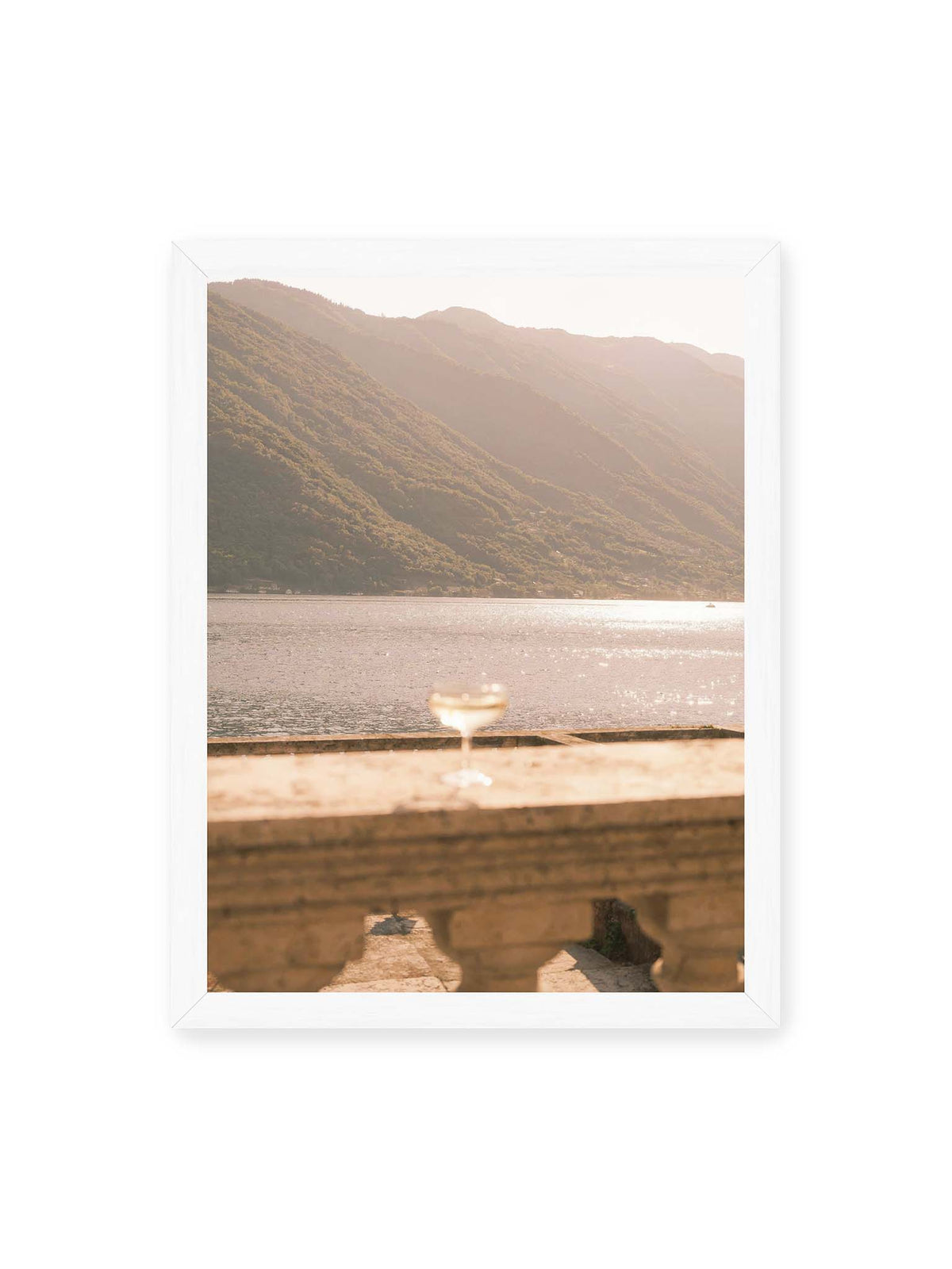 30x40 cm, weißer Rahmen – Einzelnes Glas auf heller Steinfläche vor glitzerndem Wasser und bewaldeten Berghängen.