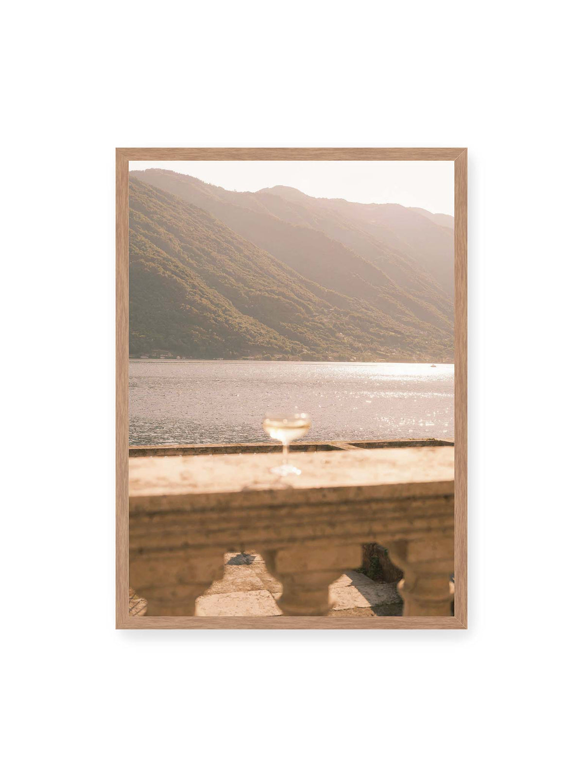 50x70 cm, Eichenrahmen – Einzelnes Glas auf heller Steinfläche vor glitzerndem Wasser und bewaldeten Berghängen.