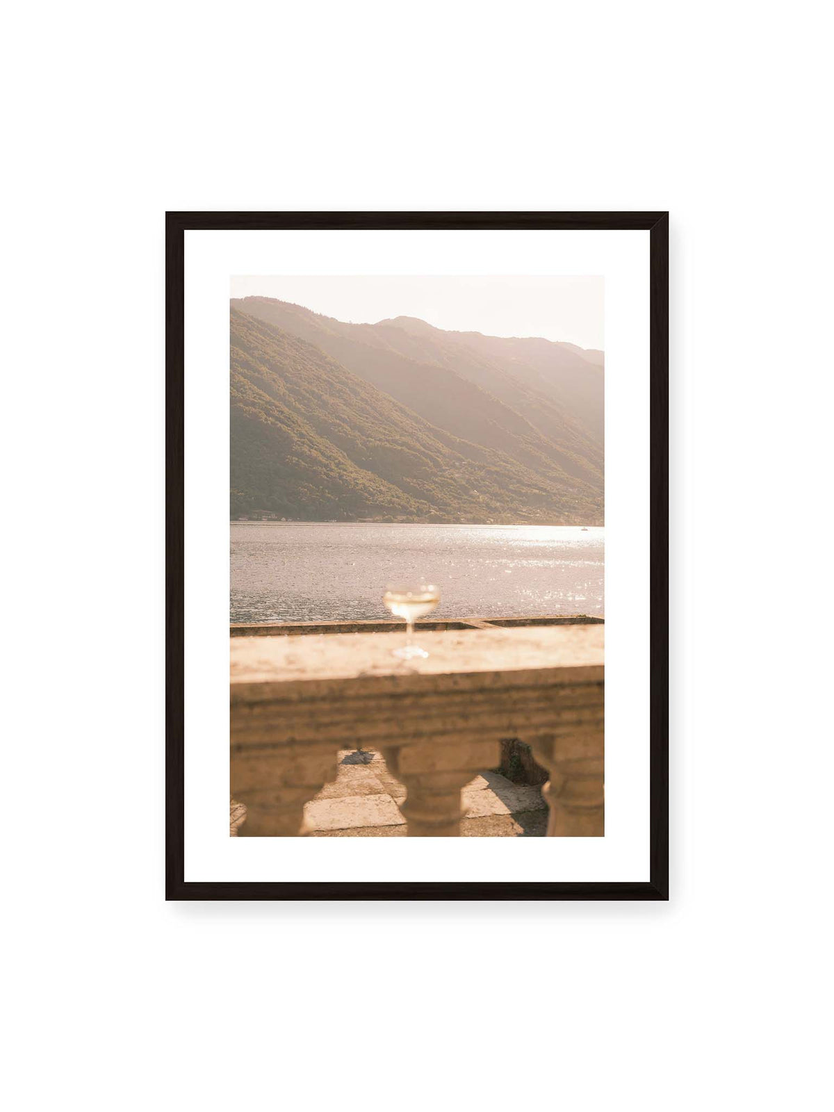 50x70 cm, weißer Galerie-Rand, schwarzer Rahmen – Einzelnes Glas auf heller Steinfläche vor glitzerndem Wasser und bewaldeten Berghängen.