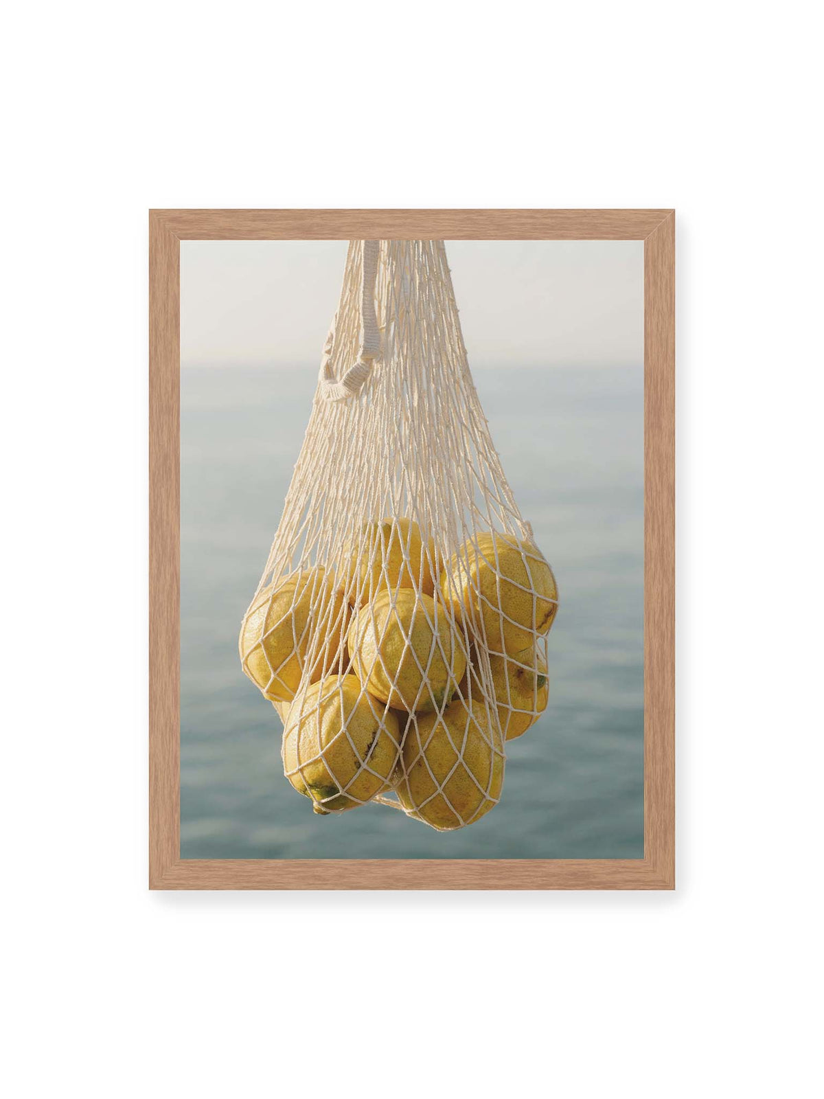 30x40 cm, Eichenrahmen – Gelbe Zitronen in einem hellen geknüpften Netz vor einer weich verschwimmenden blauen Wasserfläche.