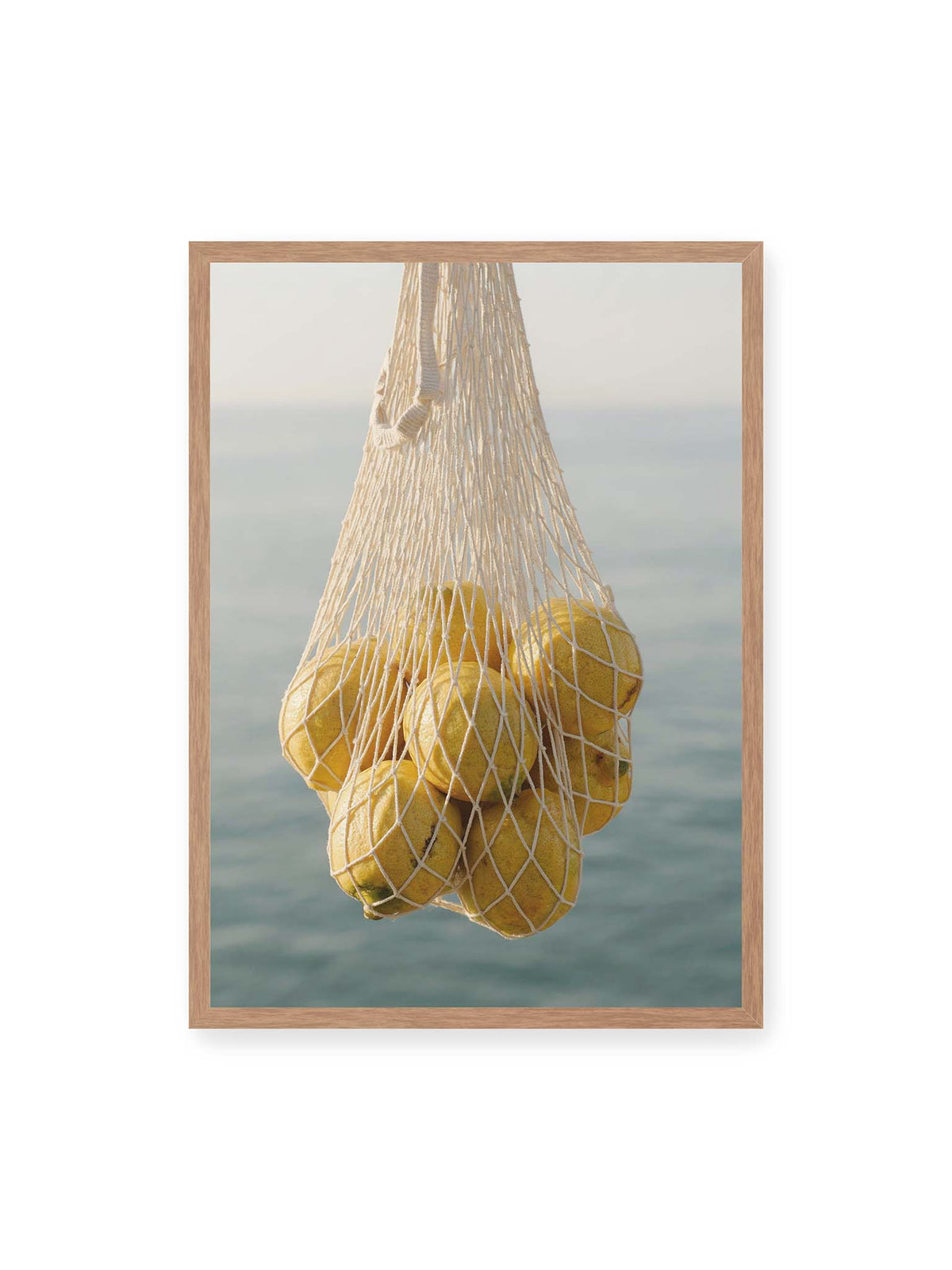50x70 cm, Eichenrahmen – Gelbe Zitronen in einem hellen geknüpften Netz vor einer weich verschwimmenden blauen Wasserfläche.