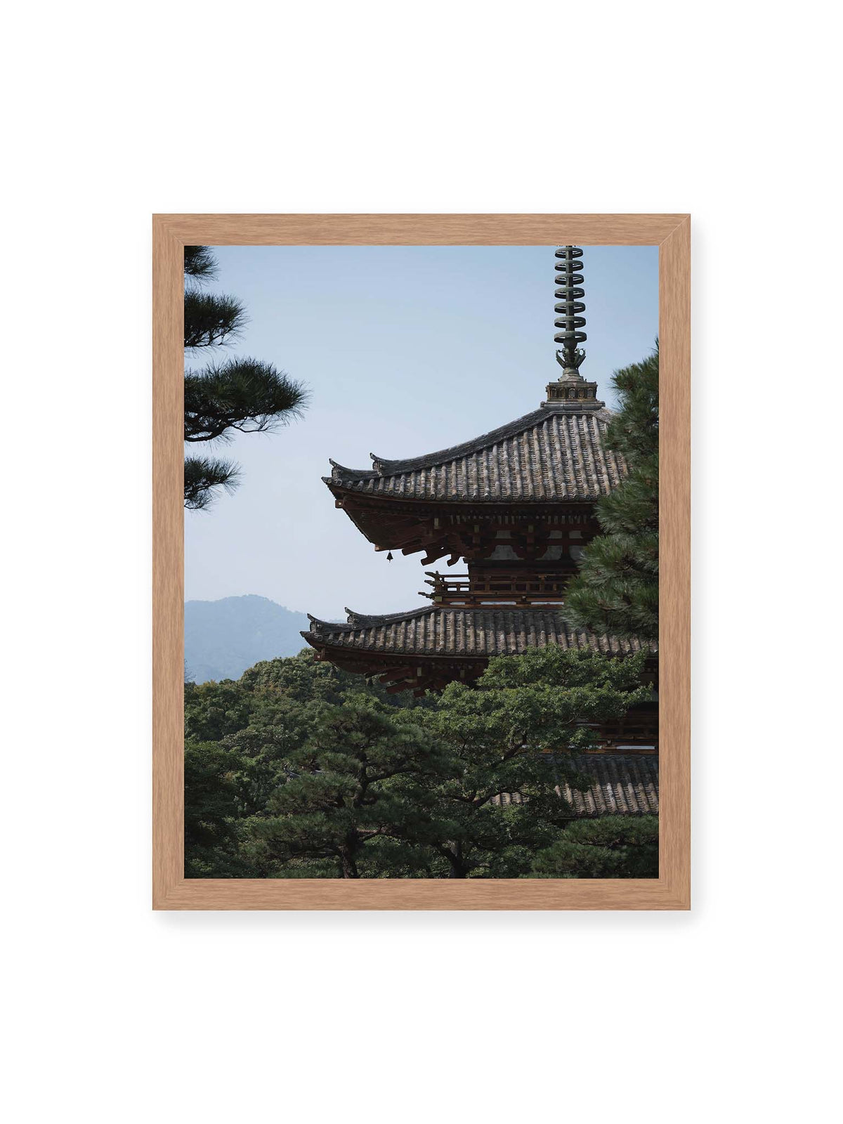 30x40 cm, Eichenrahmen – Mehrstufige Pagode mit geschwungenen Ziegeldächern zwischen dichten Kiefern vor einer blassen Bergsilhouette.