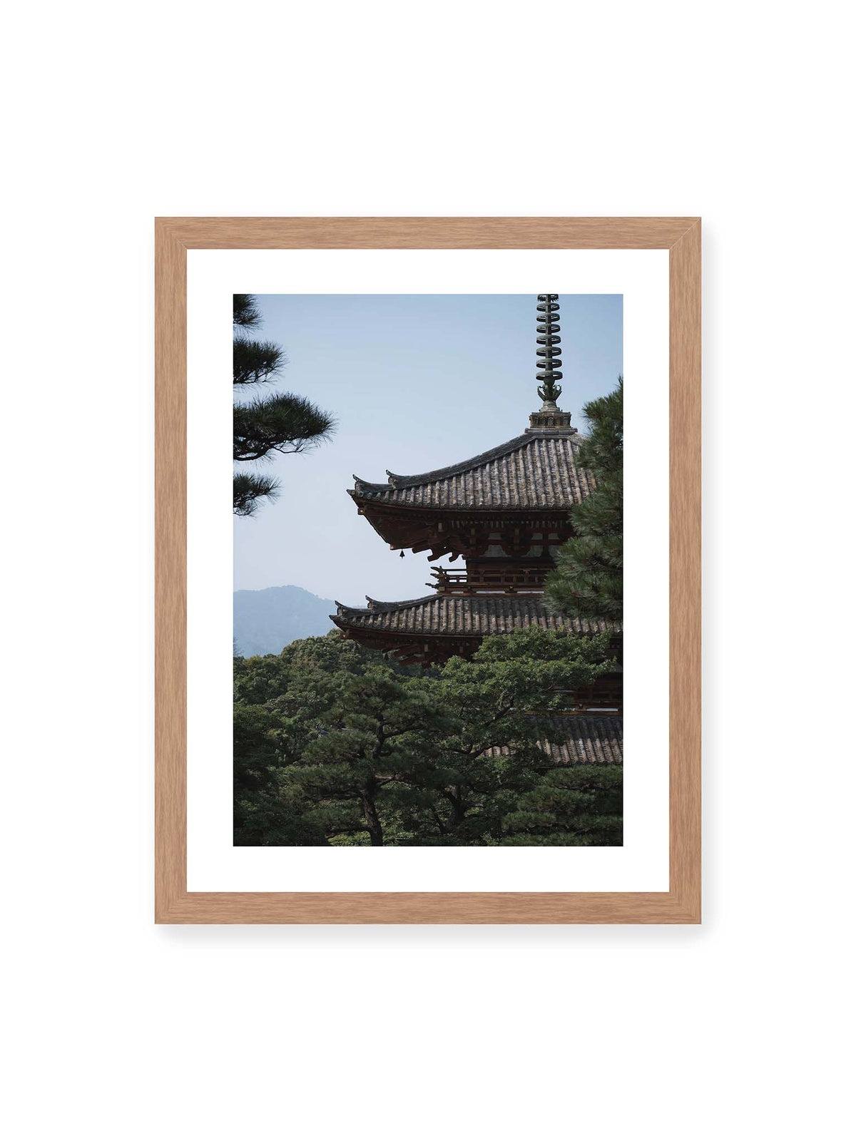 30x40 cm, weißer Galerie-Rand, Eichenrahmen – Mehrstufige Pagode mit geschwungenen Ziegeldächern zwischen dichten Kiefern vor einer blassen Bergsilhouette.