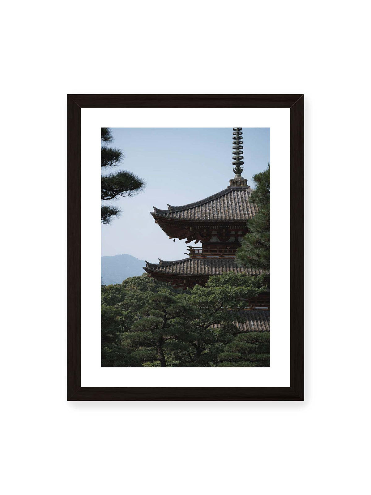 30x40 cm, weißer Galerie-Rand, schwarzer Rahmen – Mehrstufige Pagode mit geschwungenen Ziegeldächern zwischen dichten Kiefern vor einer blassen Bergsilhouette.