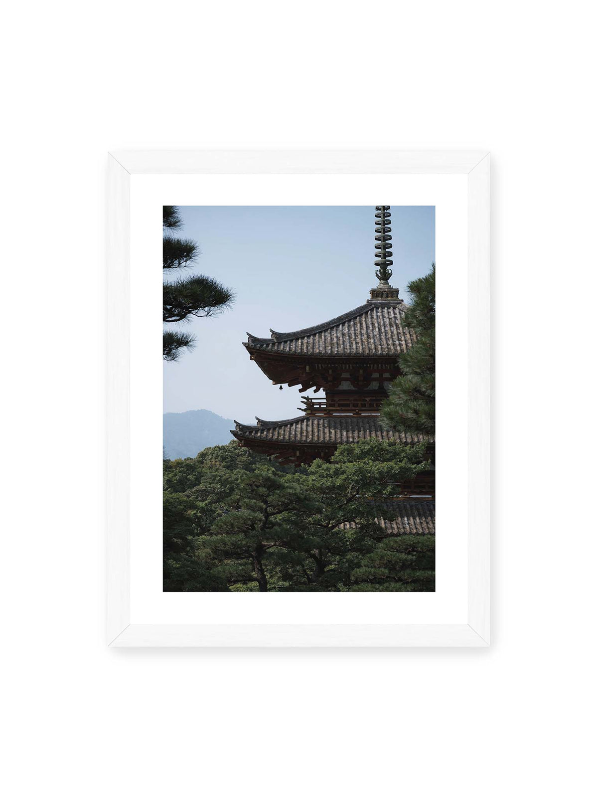 30x40 cm, weißer Galerie-Rand, weißer Rahmen – Mehrstufige Pagode mit geschwungenen Ziegeldächern zwischen dichten Kiefern vor einer blassen Bergsilhouette.