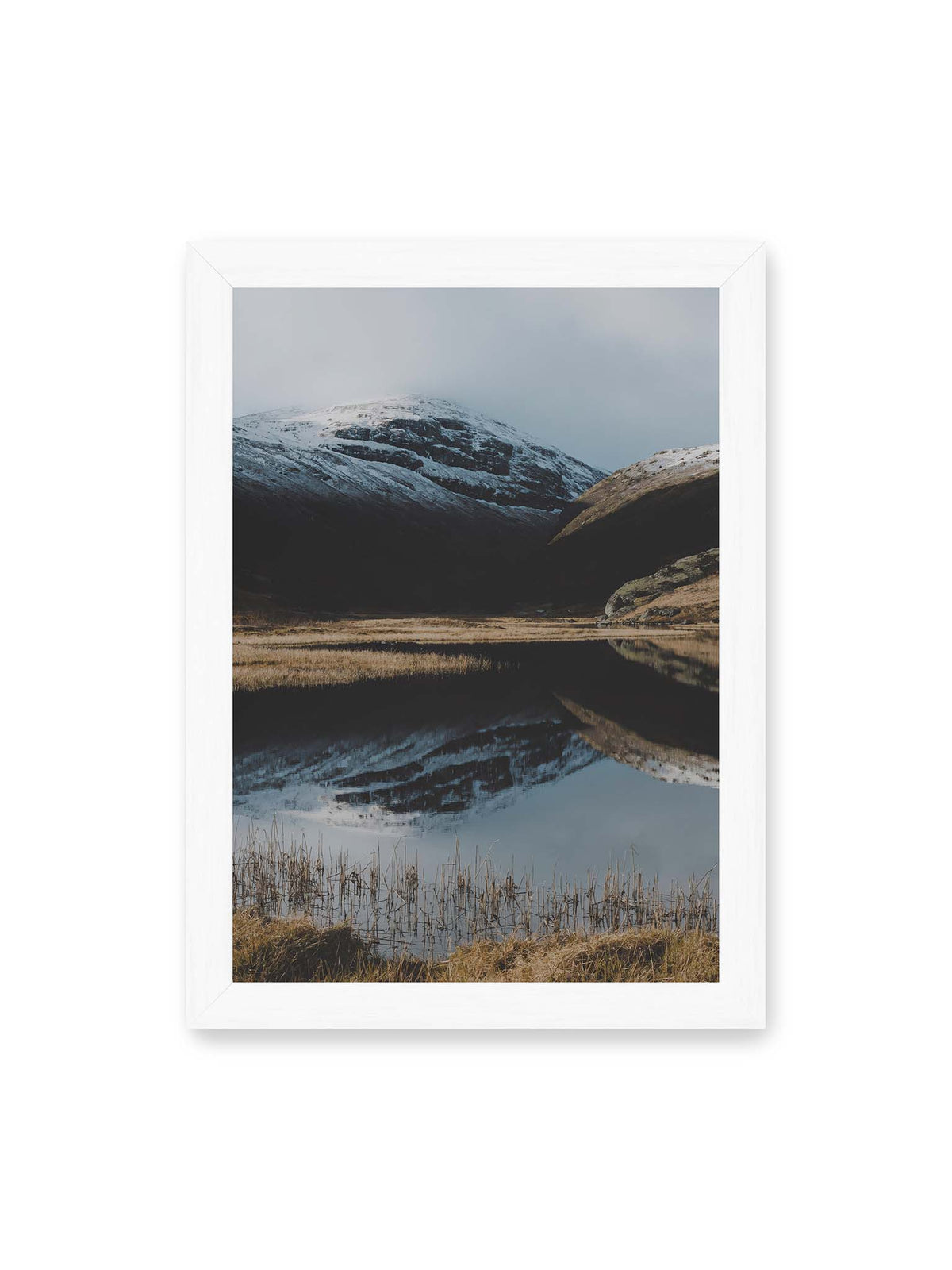 21x30 cm, weißer Rahmen – Schneebedeckte Berghänge spiegeln sich in einem stillen Gewässer, umgeben von hellen Gräsern und Schilf.