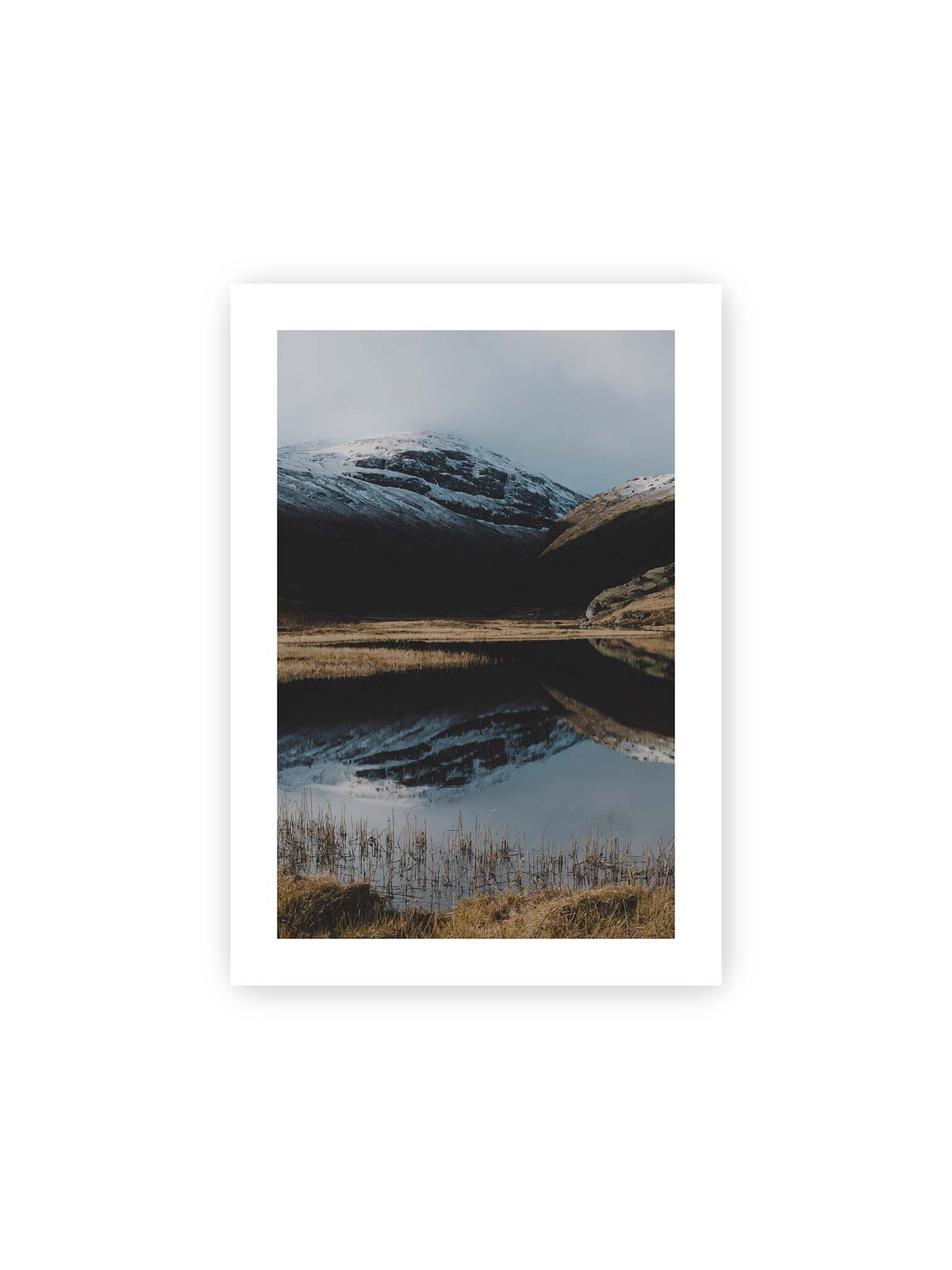 21x30 cm, weißer Galerie-Rand – Schneebedeckte Berghänge spiegeln sich in einem stillen Gewässer, umgeben von hellen Gräsern und Schilf.