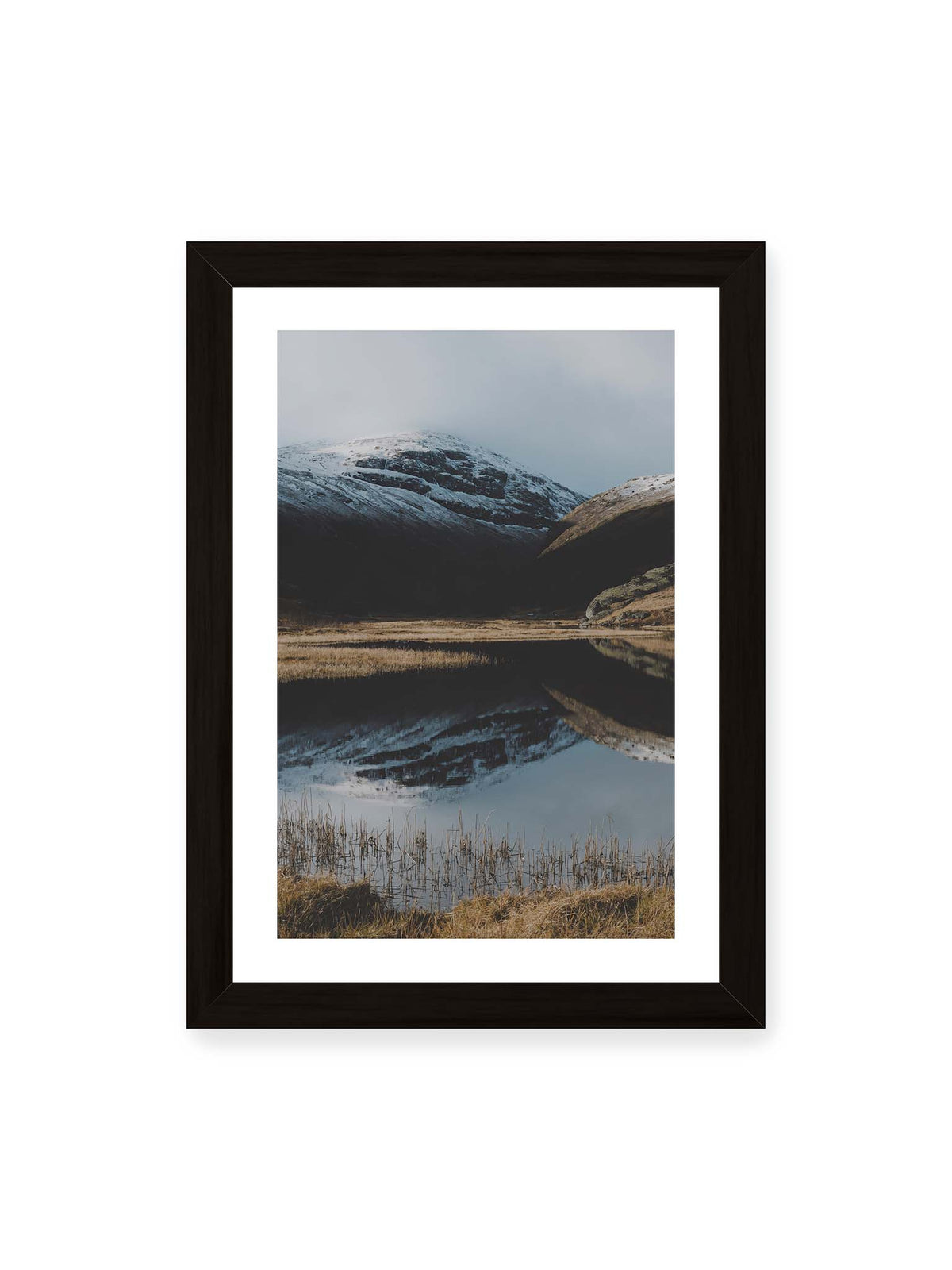 21x30 cm, weißer Galerie-Rand, schwarzer Rahmen – Schneebedeckte Berghänge spiegeln sich in einem stillen Gewässer, umgeben von hellen Gräsern und Schilf.