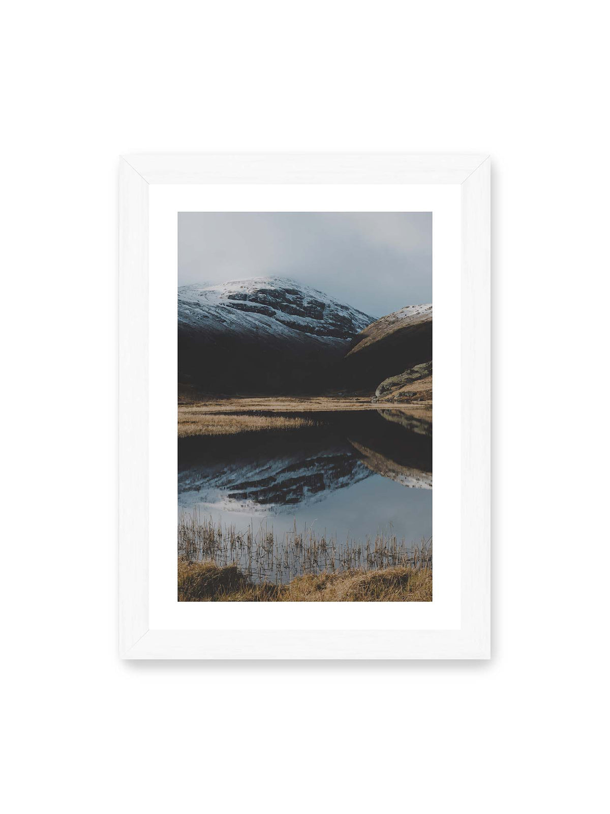 21x30 cm, weißer Galerie-Rand, weißer Rahmen – Schneebedeckte Berghänge spiegeln sich in einem stillen Gewässer, umgeben von hellen Gräsern und Schilf.