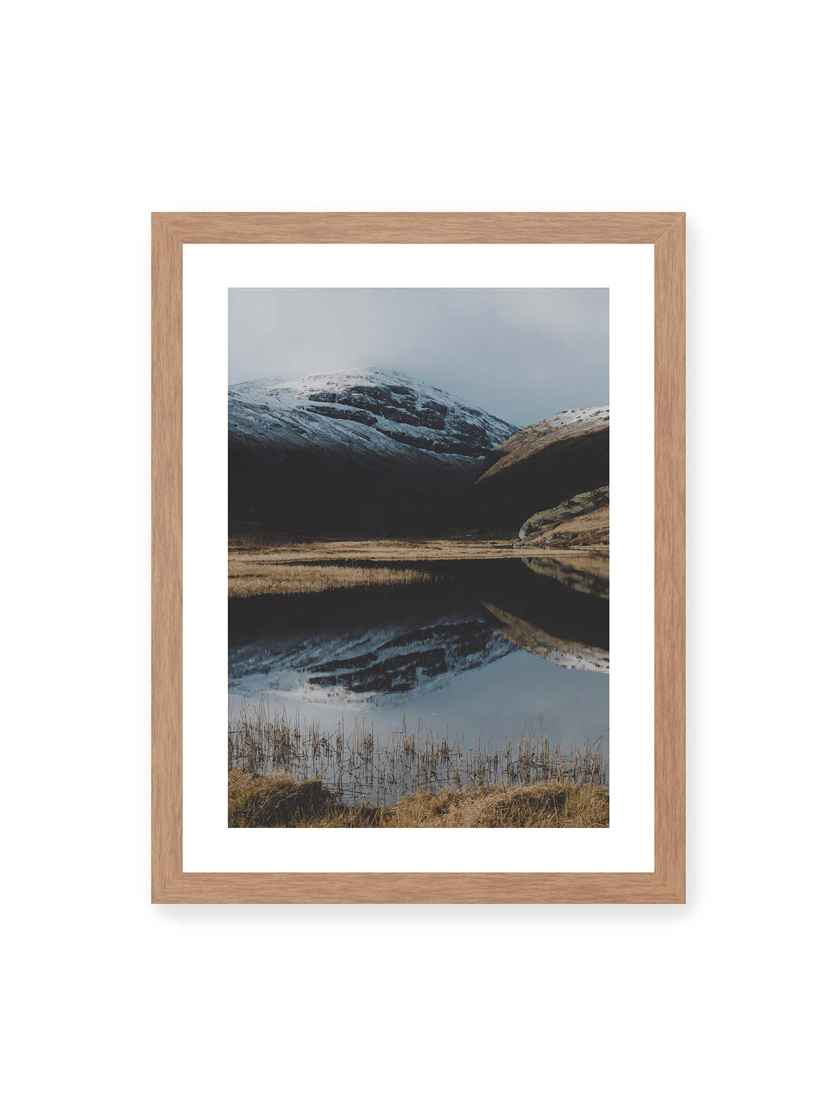 30x40 cm, weißer Galerie-Rand, Eichenrahmen – Schneebedeckte Berghänge spiegeln sich in einem stillen Gewässer, umgeben von hellen Gräsern und Schilf.