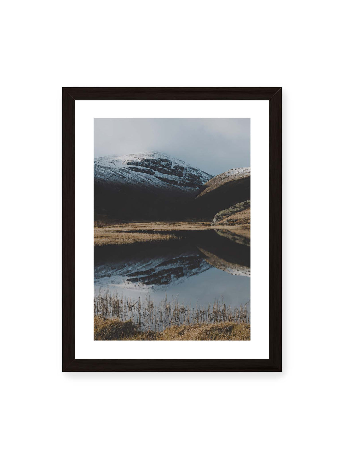 30x40 cm, weißer Galerie-Rand, schwarzer Rahmen – Schneebedeckte Berghänge spiegeln sich in einem stillen Gewässer, umgeben von hellen Gräsern und Schilf.