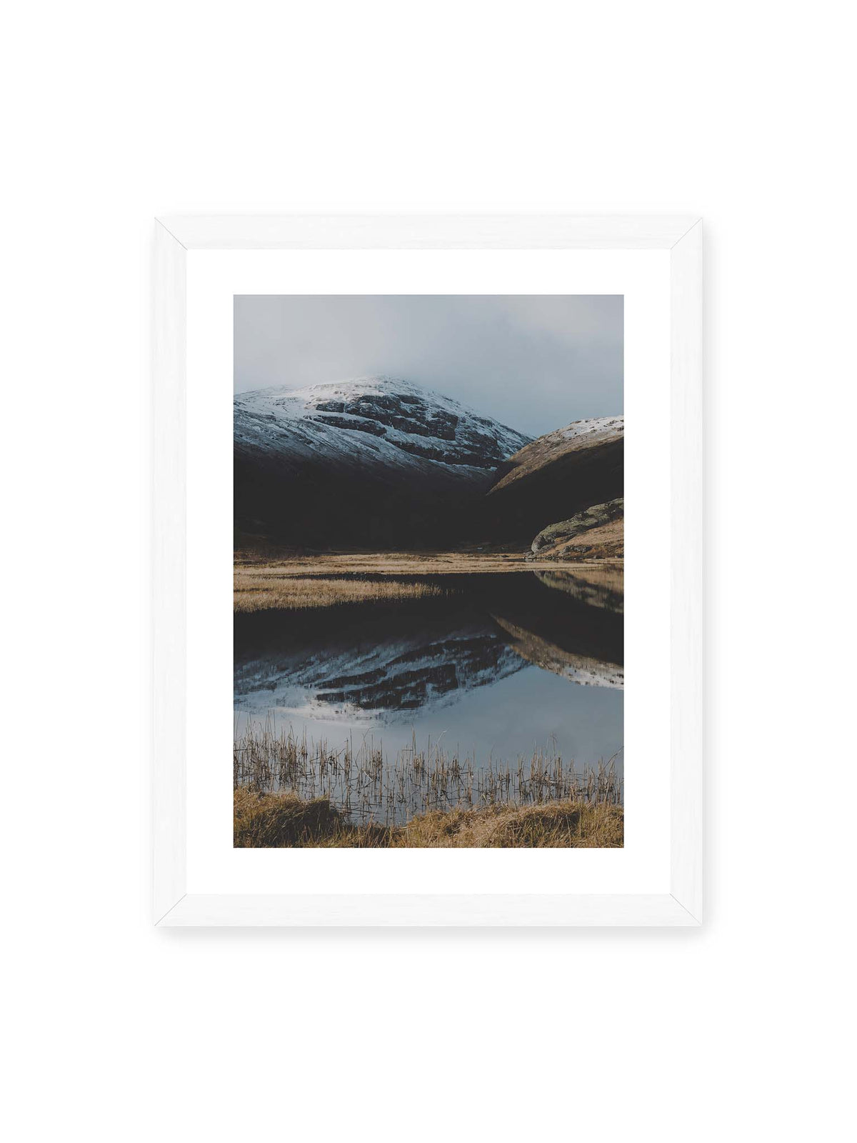 30x40 cm, weißer Galerie-Rand, weißer Rahmen – Schneebedeckte Berghänge spiegeln sich in einem stillen Gewässer, umgeben von hellen Gräsern und Schilf.