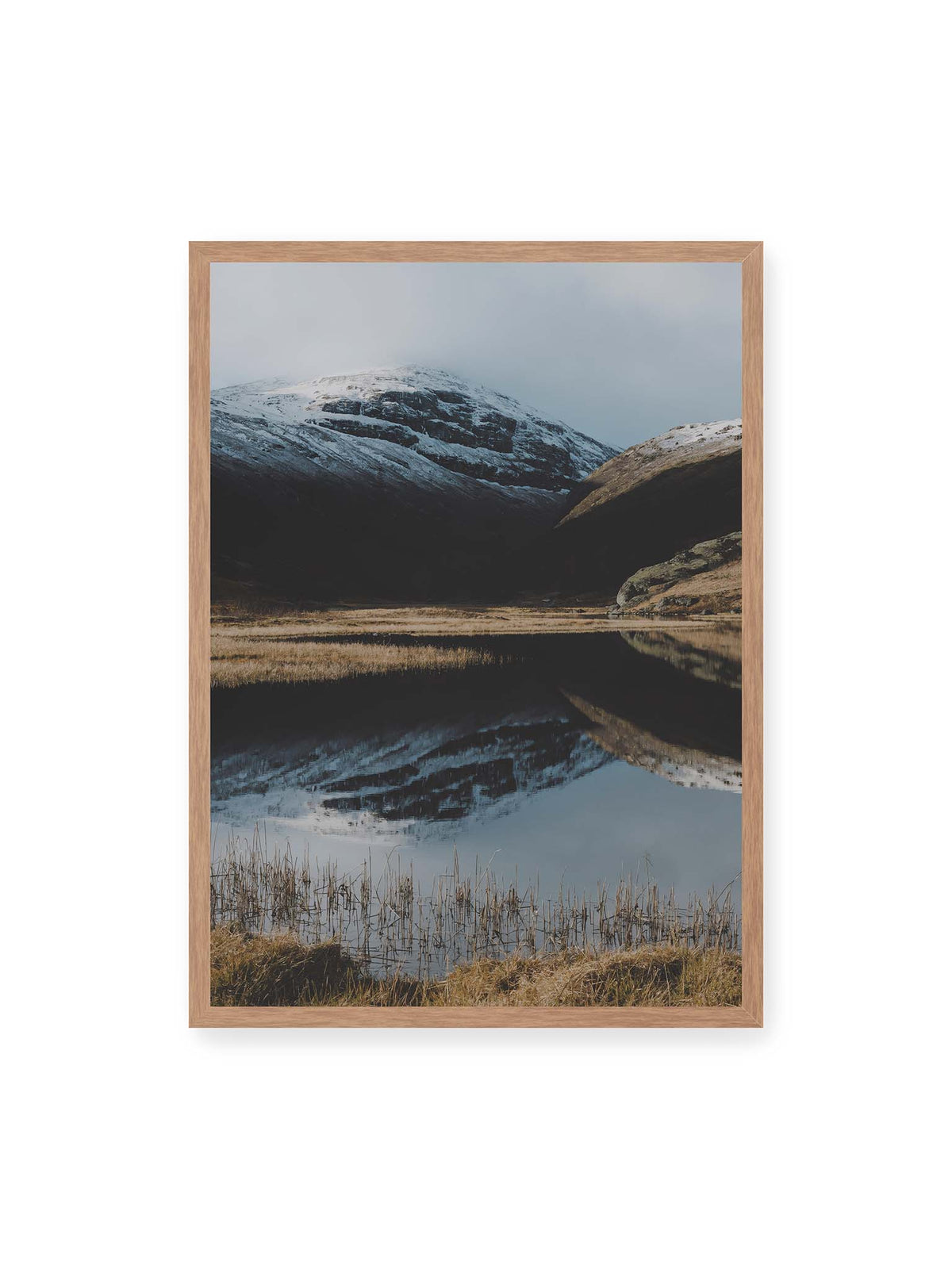 50x70 cm, Eichenrahmen – Schneebedeckte Berghänge spiegeln sich in einem stillen Gewässer, umgeben von hellen Gräsern und Schilf.