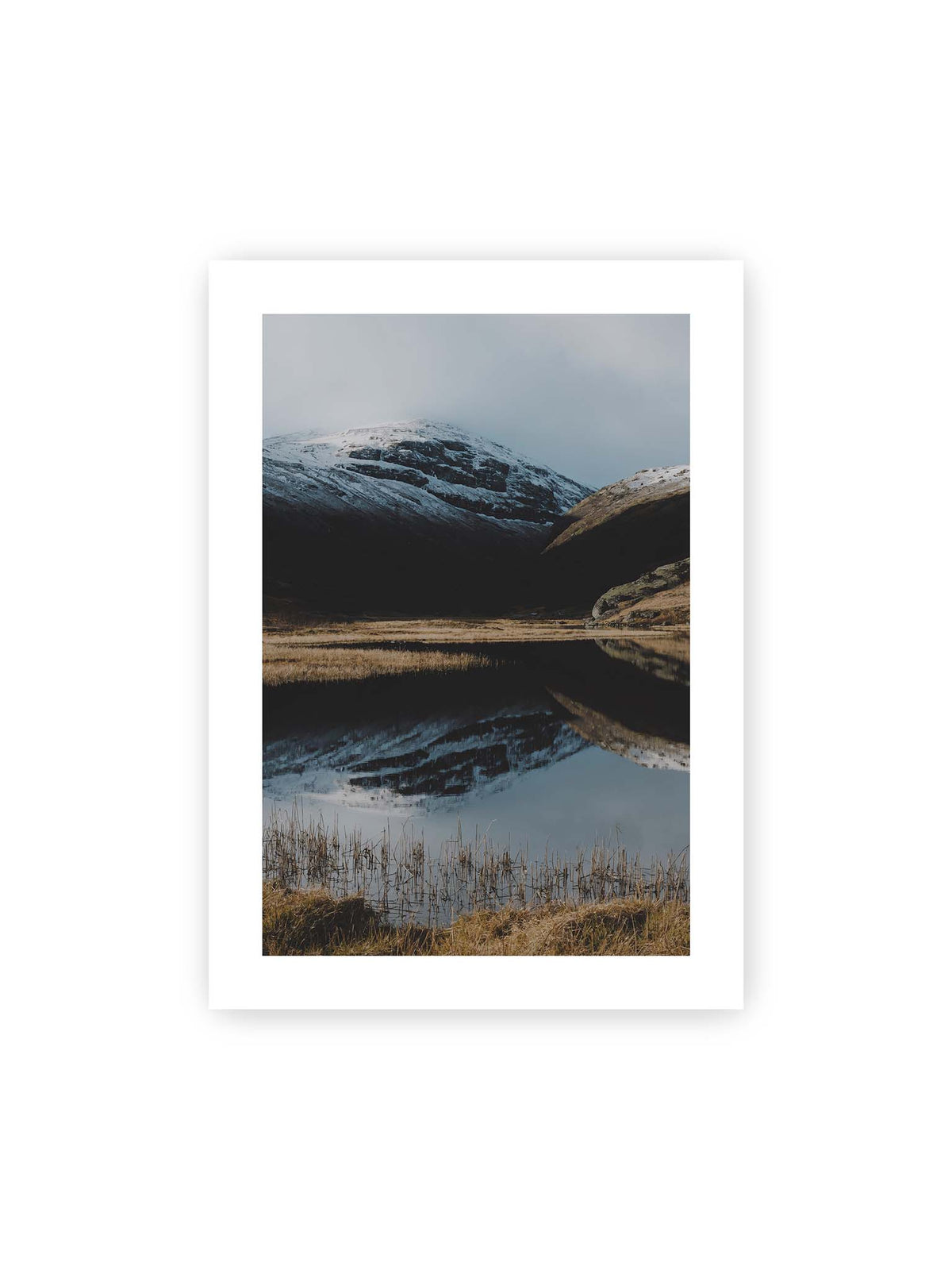 50x70 cm, weißer Galerie-Rand – Schneebedeckte Berghänge spiegeln sich in einem stillen Gewässer, umgeben von hellen Gräsern und Schilf.